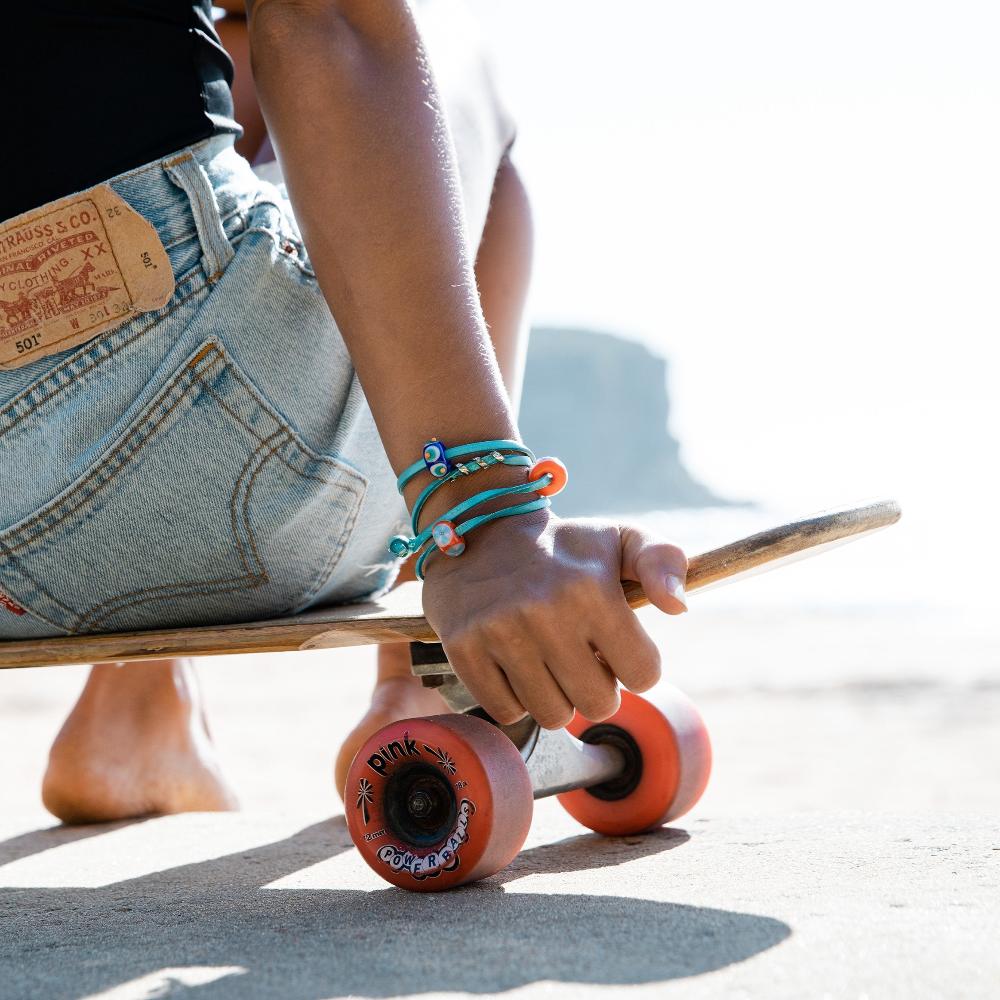 Woman sitting on a skateboard wearing a turquoise leather bracelet.