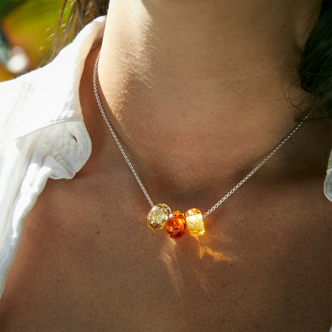 Amber sand bead trio on silver necklace worn by woman amongst plants.