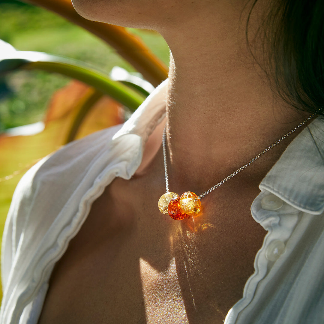 Amber sand bead trio on silver necklace worn by woman amongst plants.