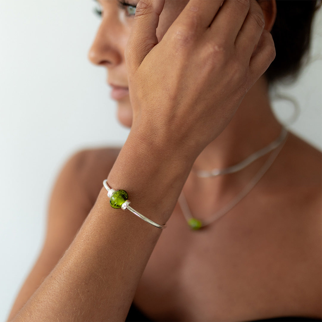 Woman wearing silver bangle with bright green sand bead.