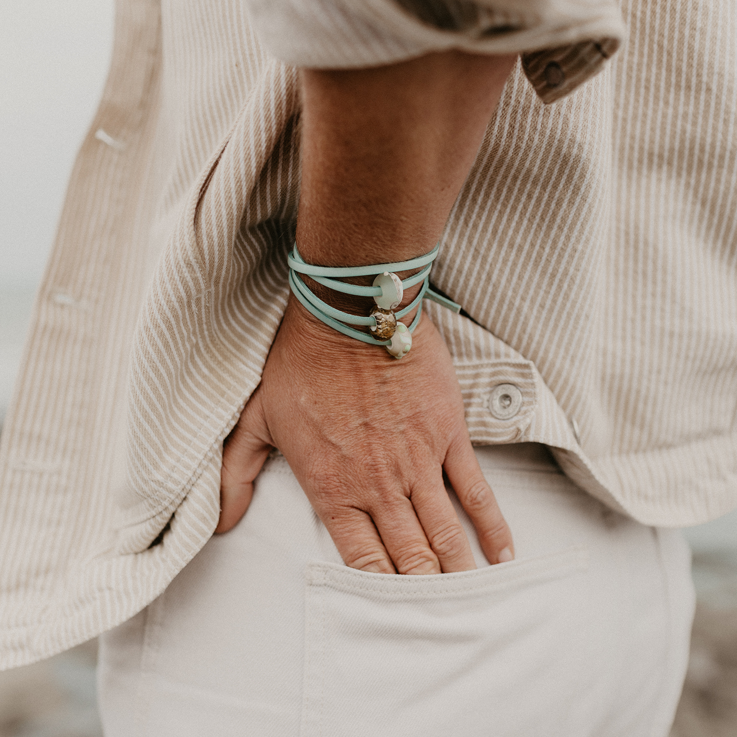 Person in cream coloured jacket and jeans wearing an aqua leather bracelet with three glass beads on it.