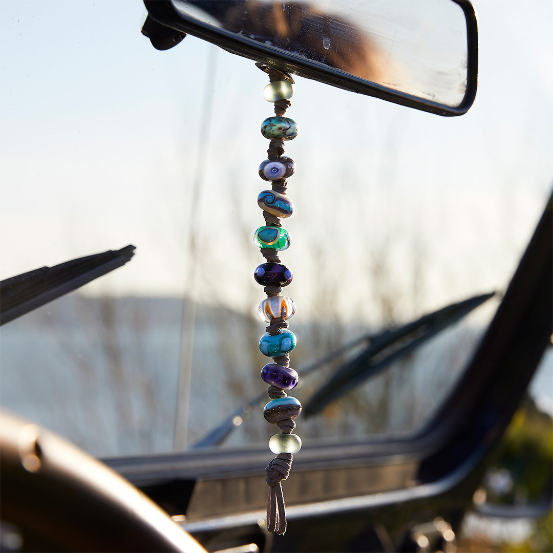 Colourful glass bead string hanging from rear view mirror in car.