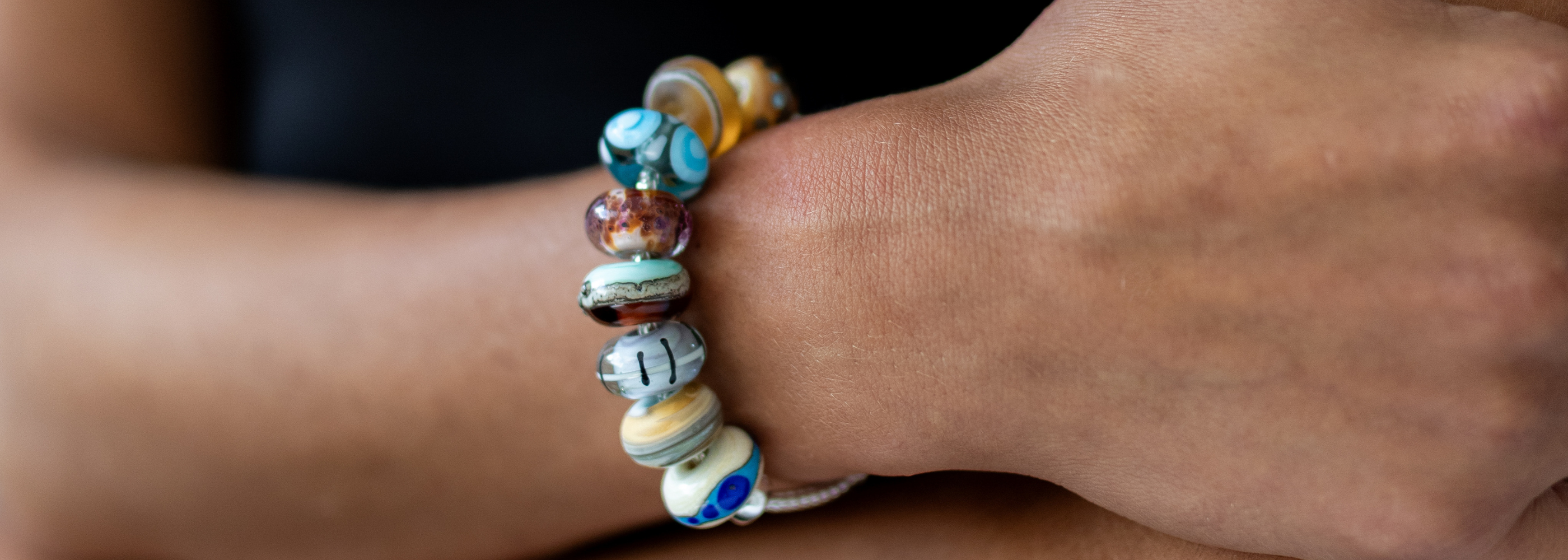 Colourful glass beads on a silver bracelet worn by a person with folded arms.
