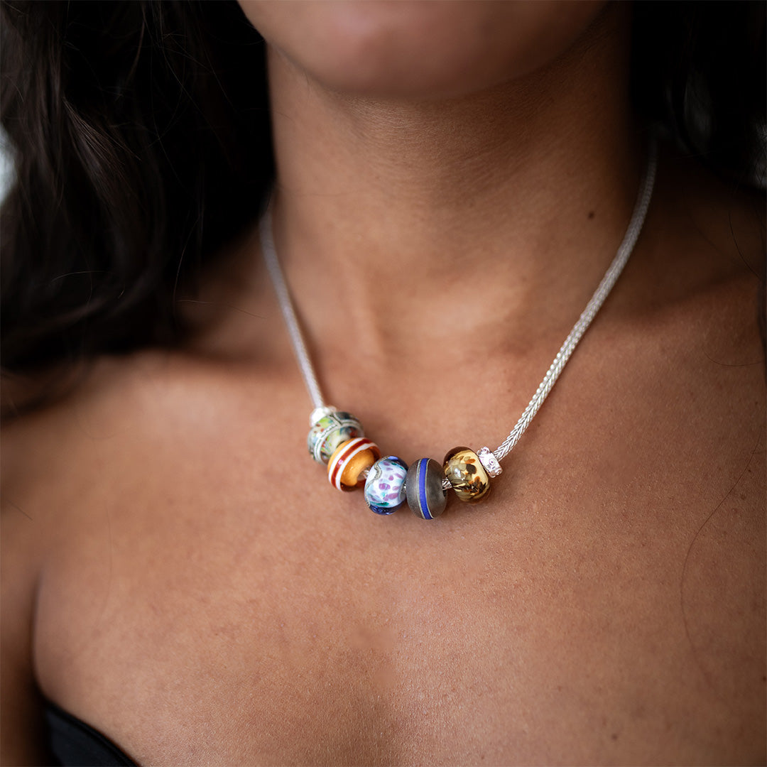 Woman wearing a black vest wearing a sterling silver necklace with blue, green patterned glass beads.