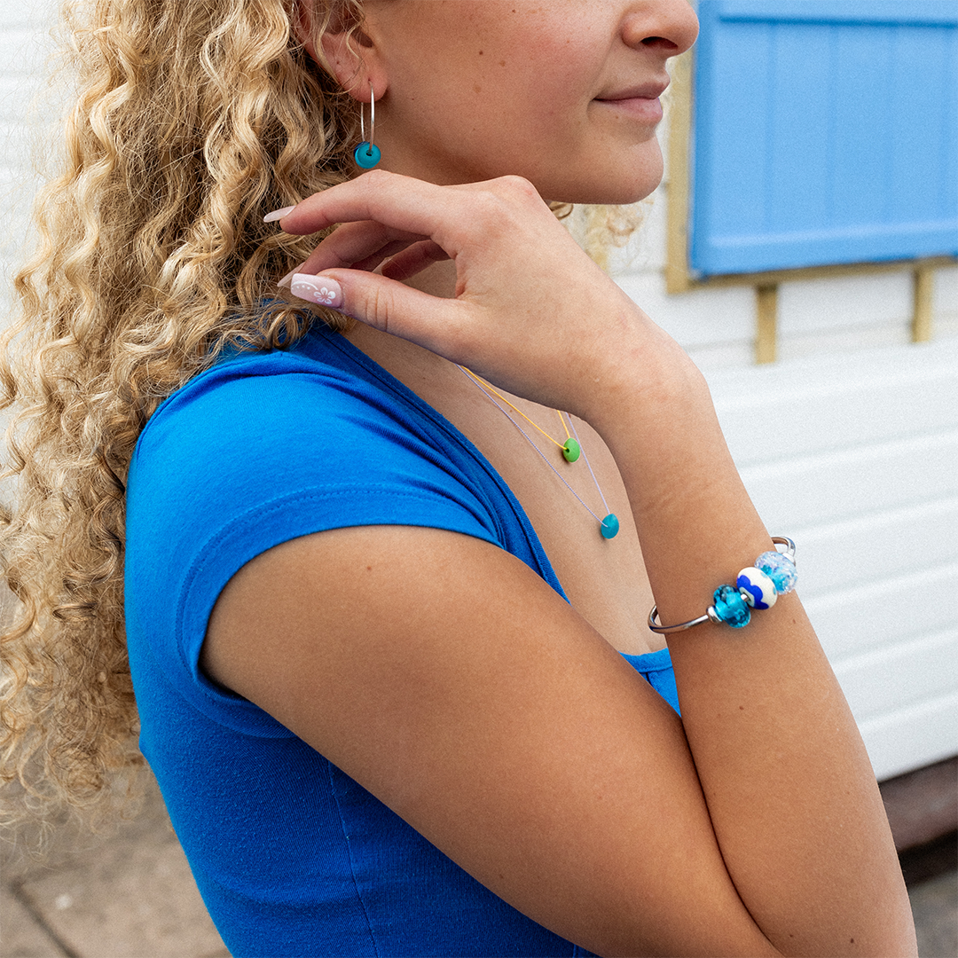 Girl wearing bangle with blue glass beads in front of beach huts on the beach.