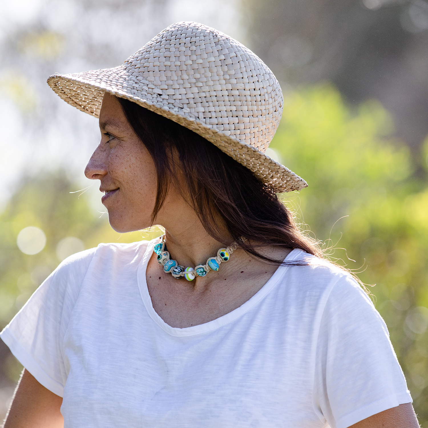 Woman in straw hat wearing sand cord choker necklace with surf glass beads.