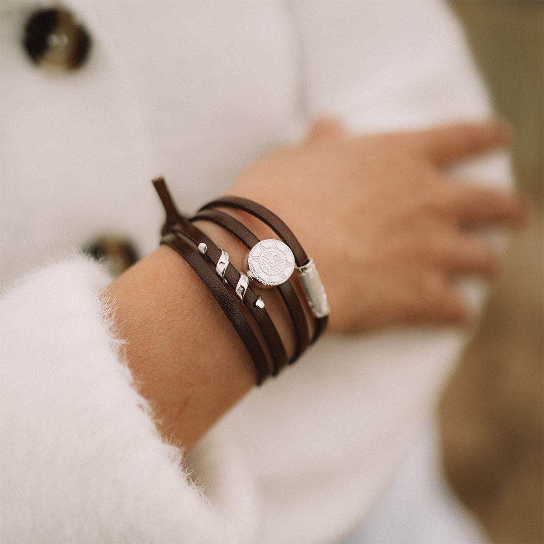 Person wearing a brown leather bracelet with silver charms on it.