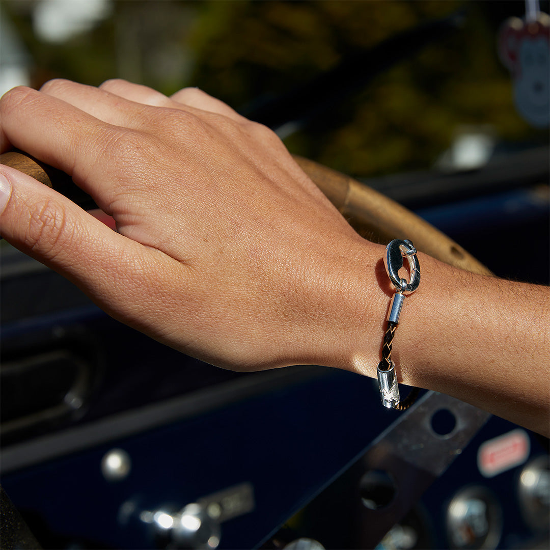 Hand on steering wheel wearing leather bracelet with silver clasp.