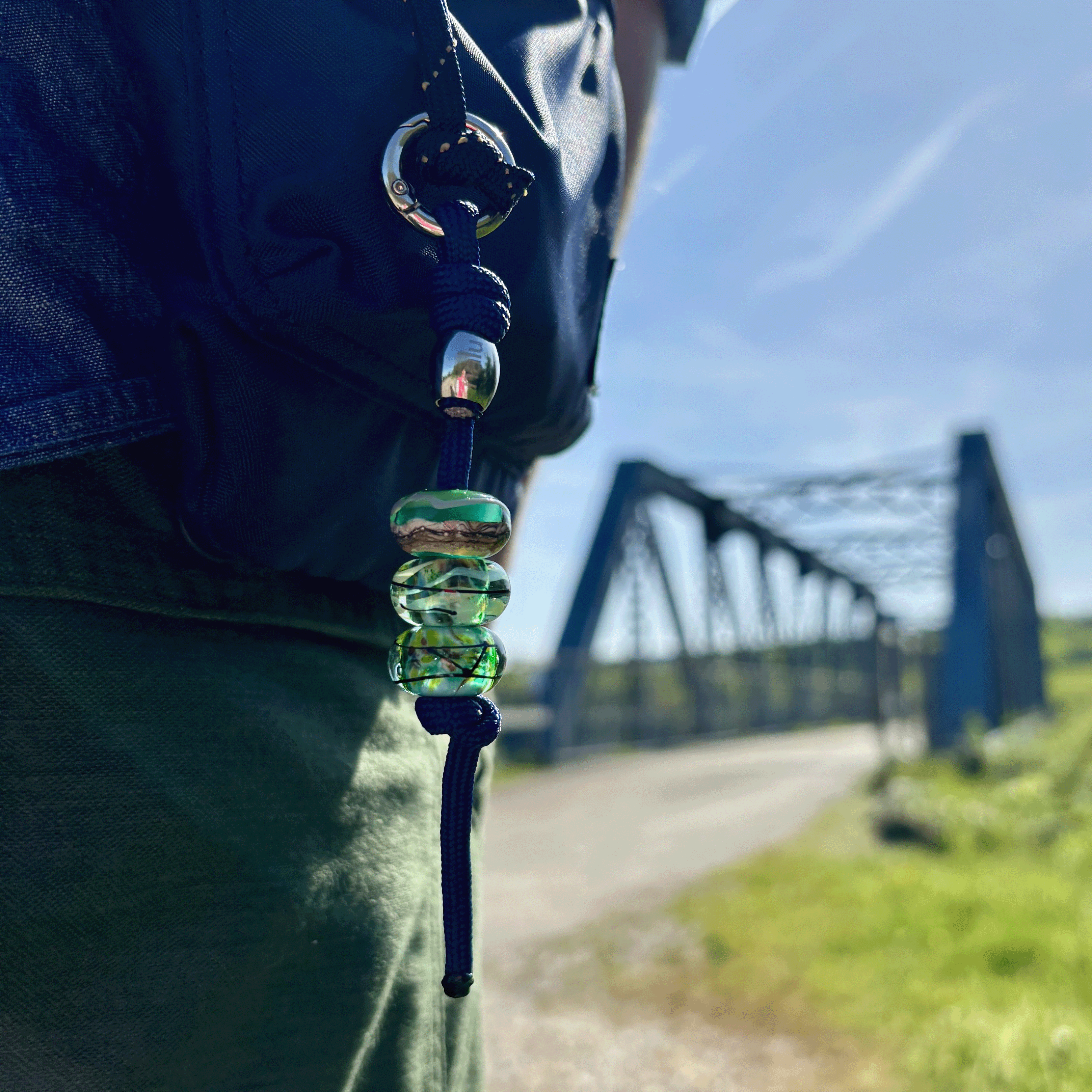 Close-up of a bag with decorative beads against a blurred background of a bridge and sky.