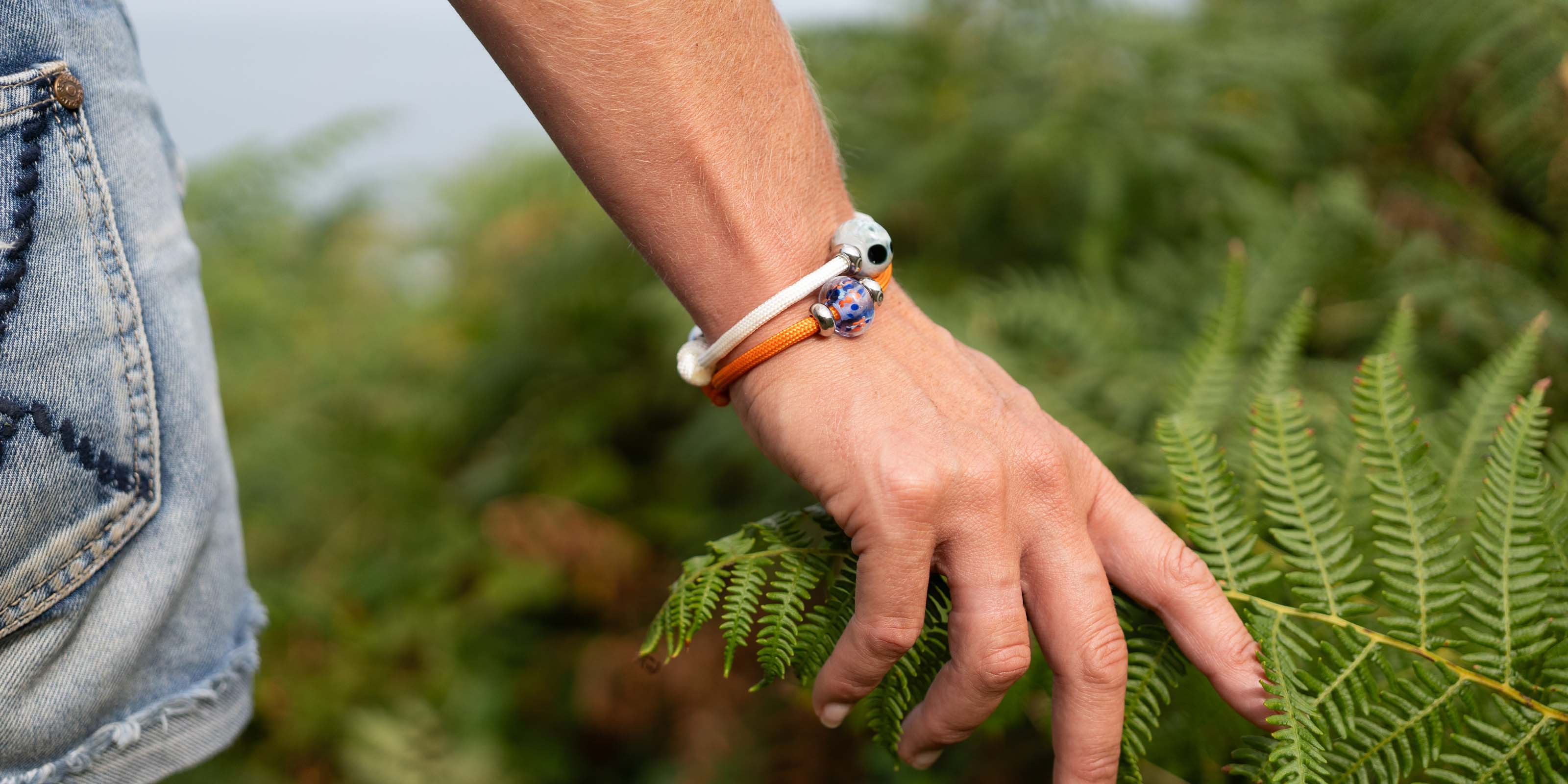 Hand with bracelets touching ferns in a natural setting