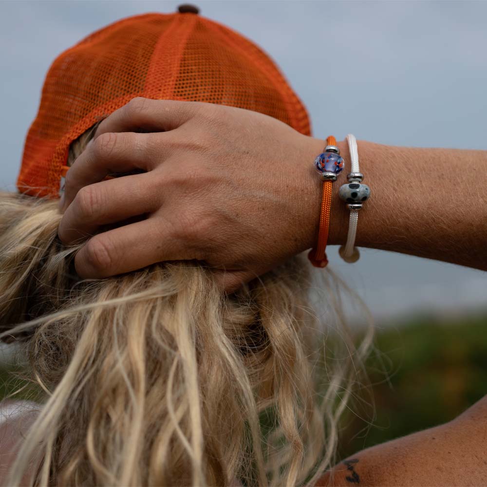 Person wearing an orange cap and multiple bracelets on a blurred natural background