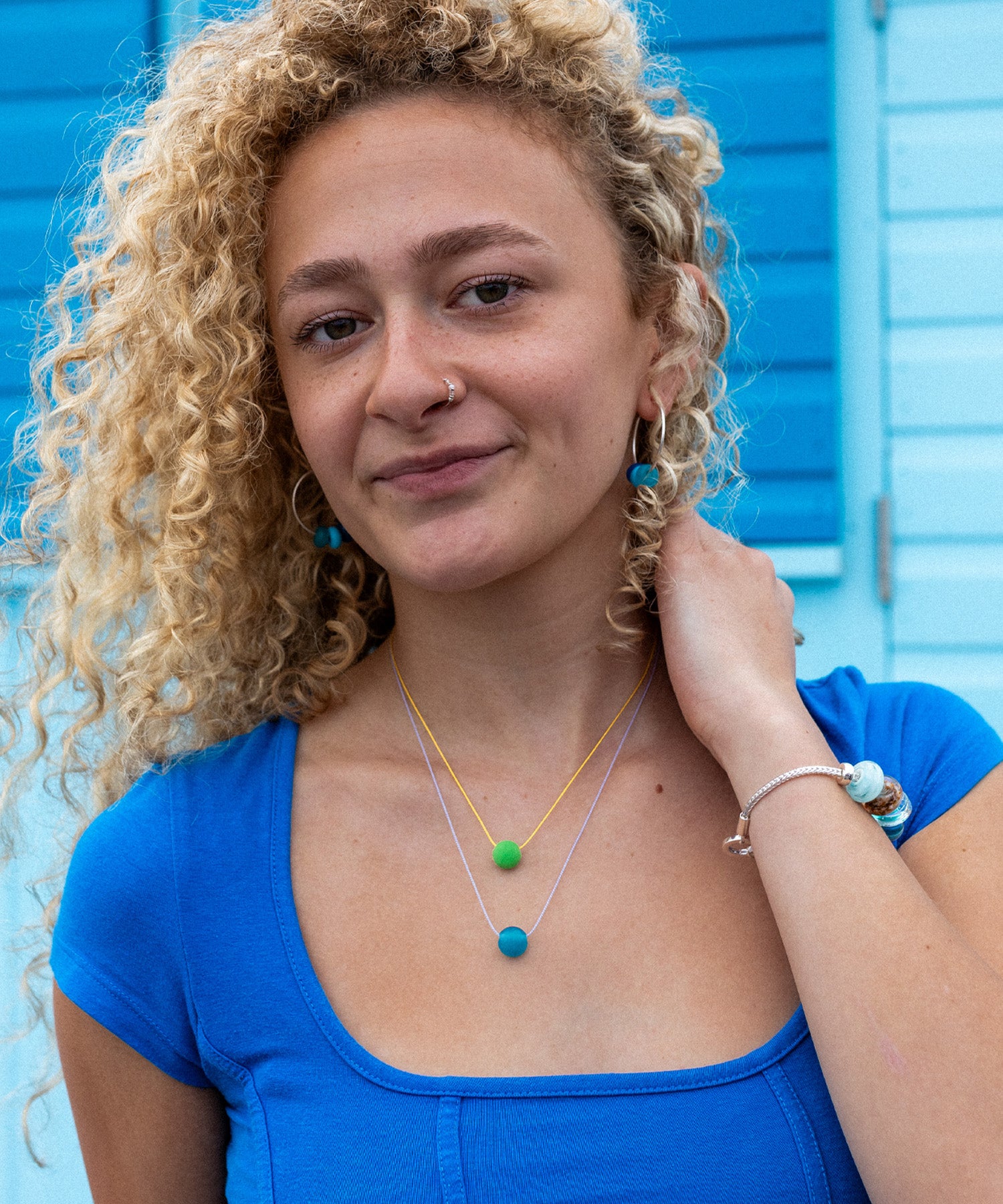 Bright blue and green colourful jewellery worn by girl next to beach huts in Devon.