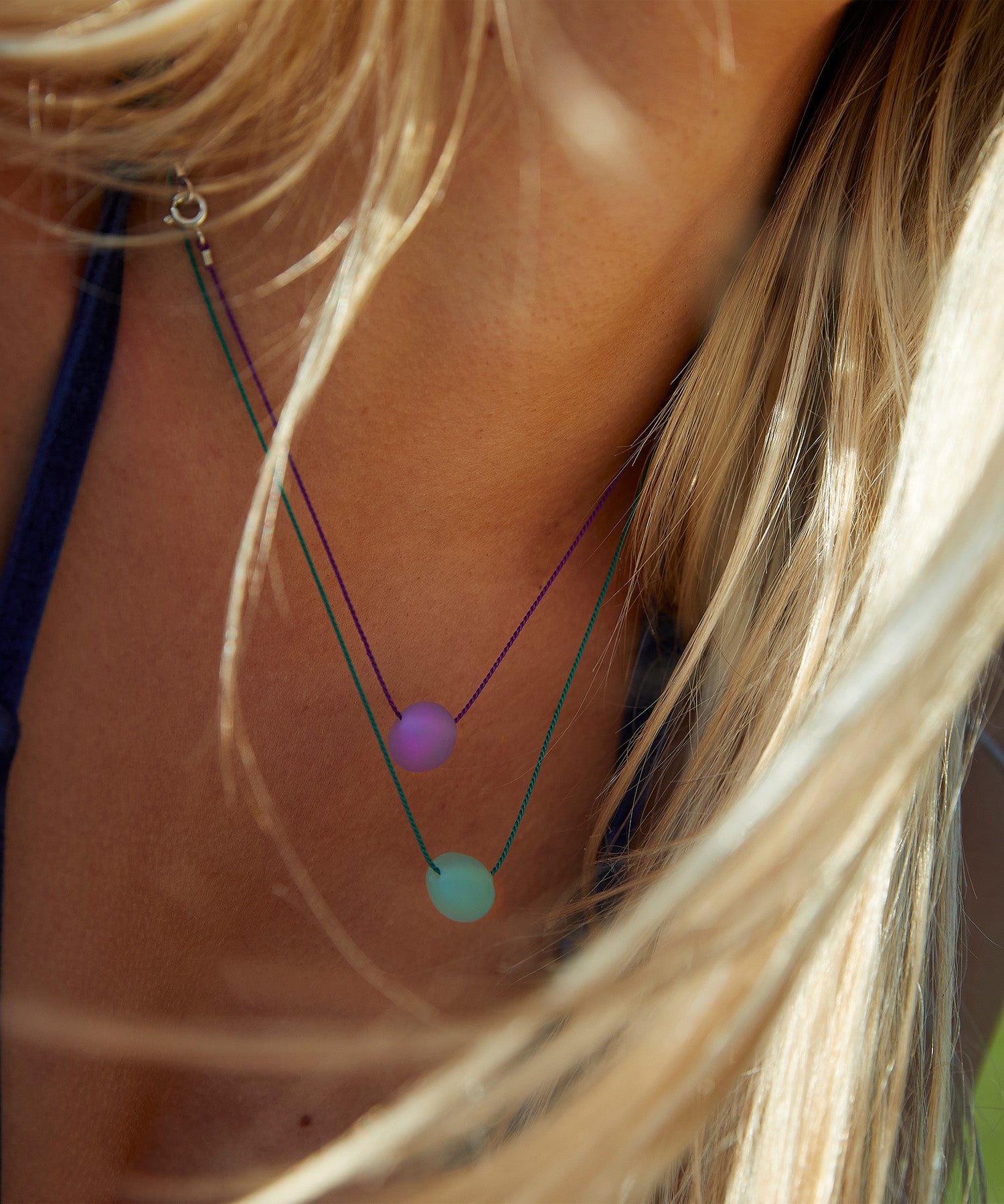 Person with long blonde hair wearing layered glass pebble necklaces in green and purple.