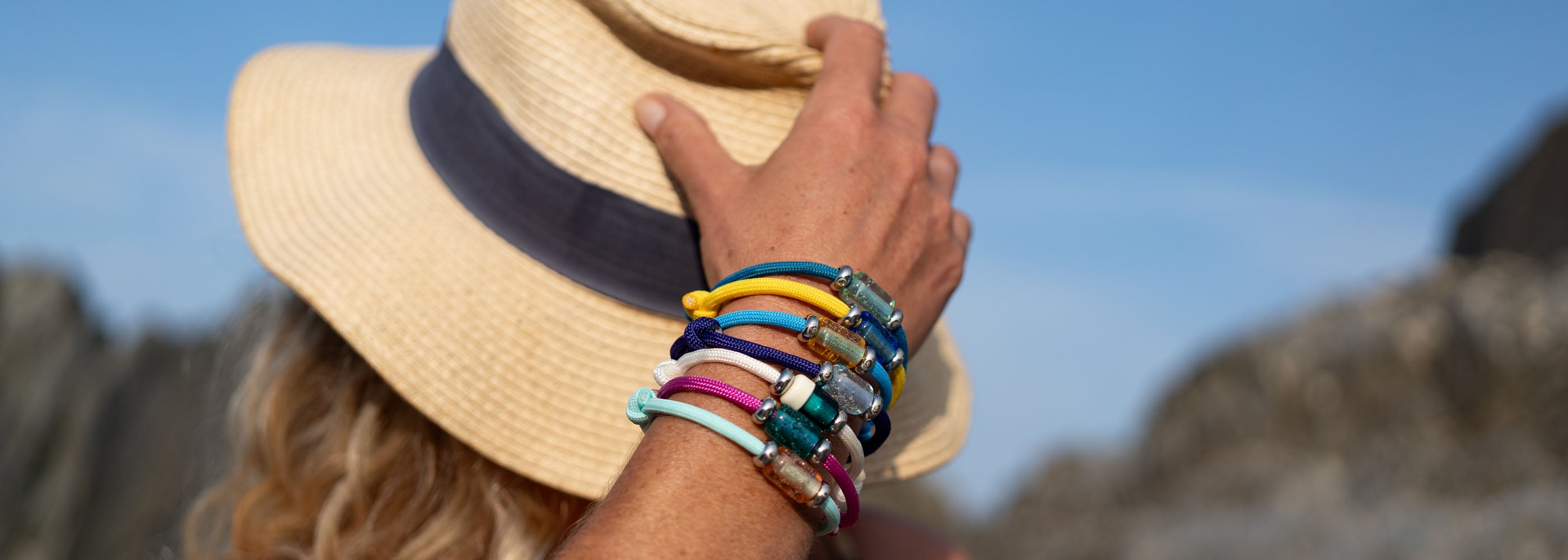 Person wearing a straw hat and colorful bracelets against a blurred natural background