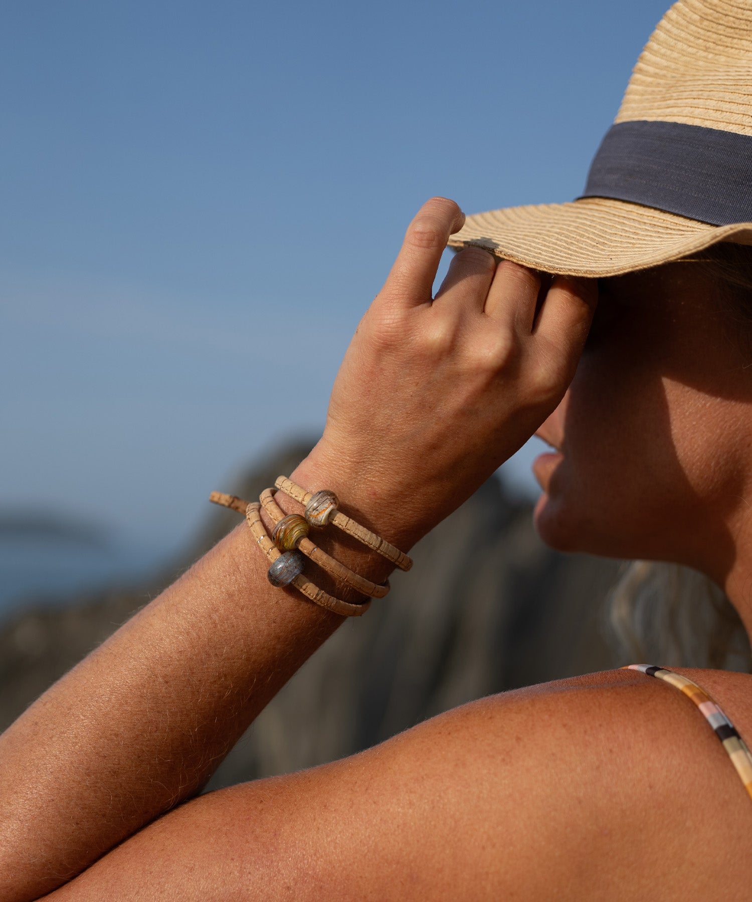 Person wearing a straw hat and multiple bracelets against a blurred natural background
