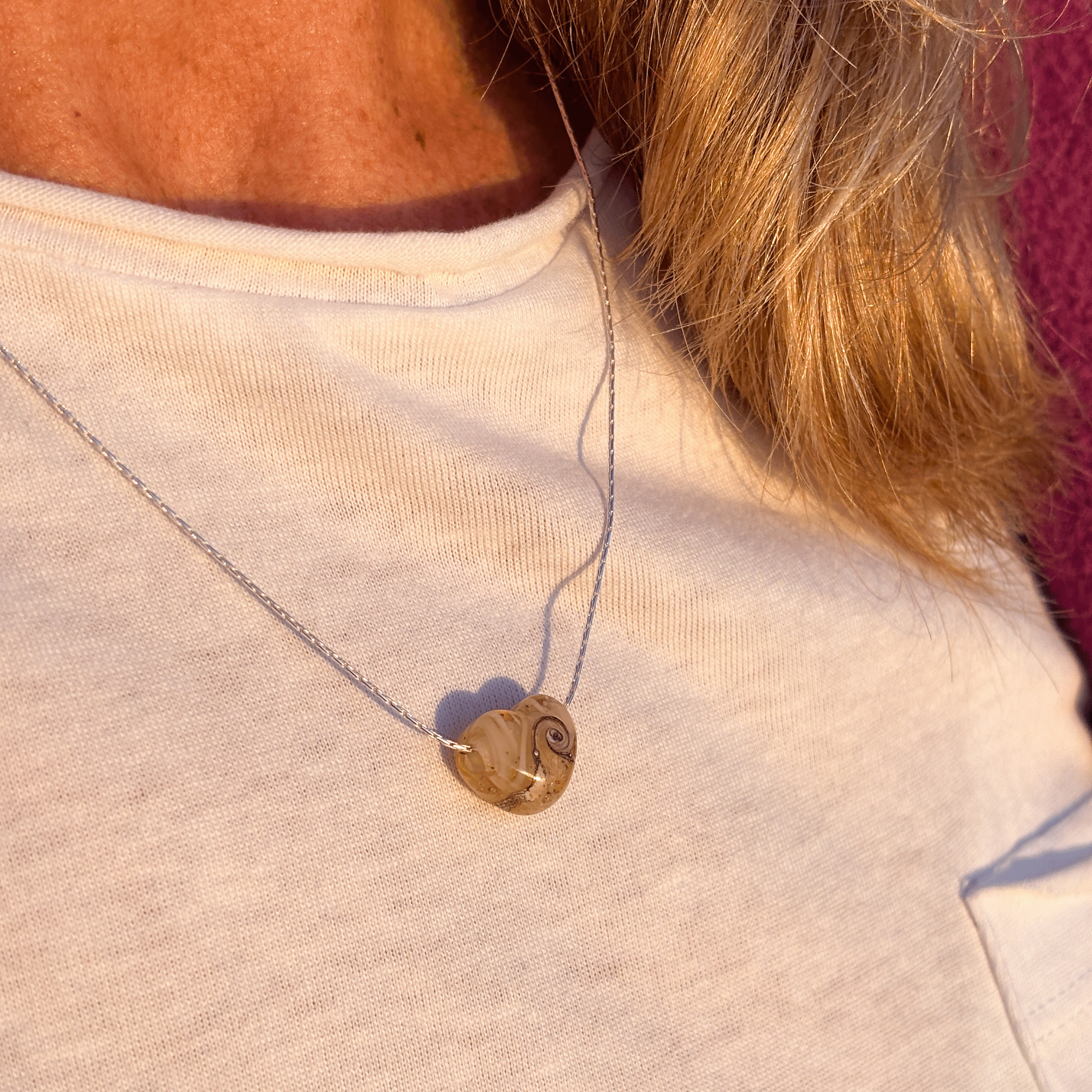 Cream sand heart necklace on silver chain worn by person.