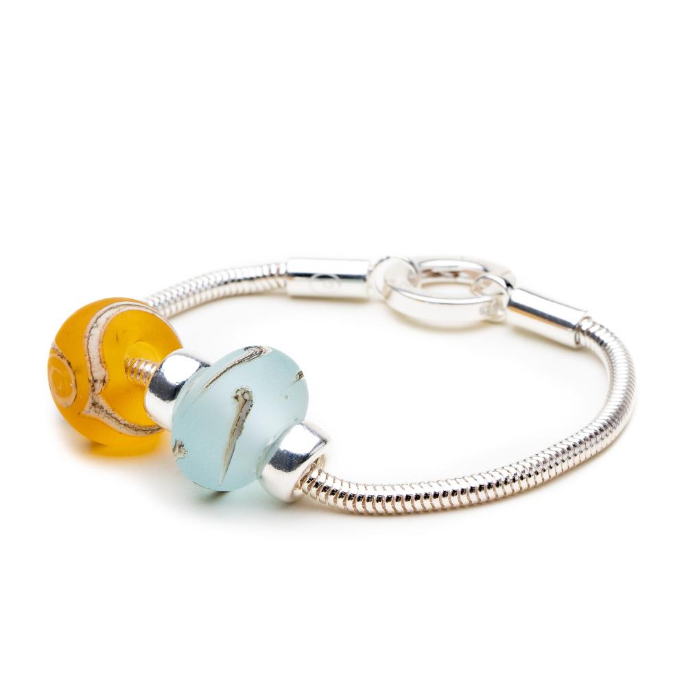 Silver snake bracelet with a blue and amber coloured glass bead worn on it.