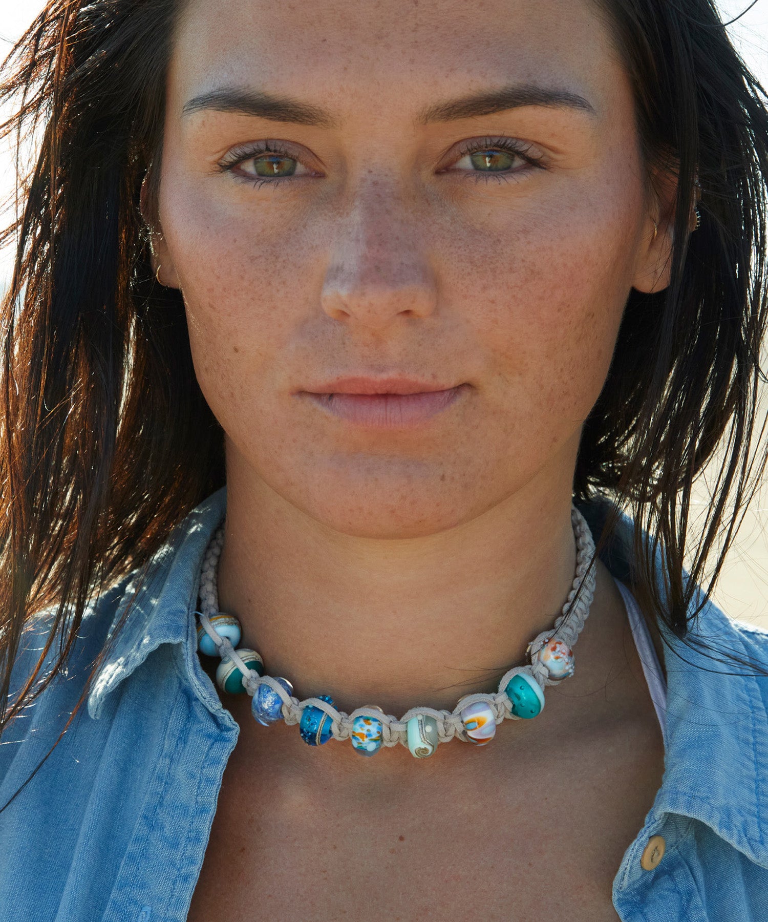 Dark haired woman wearing a beaded choker cord necklace.