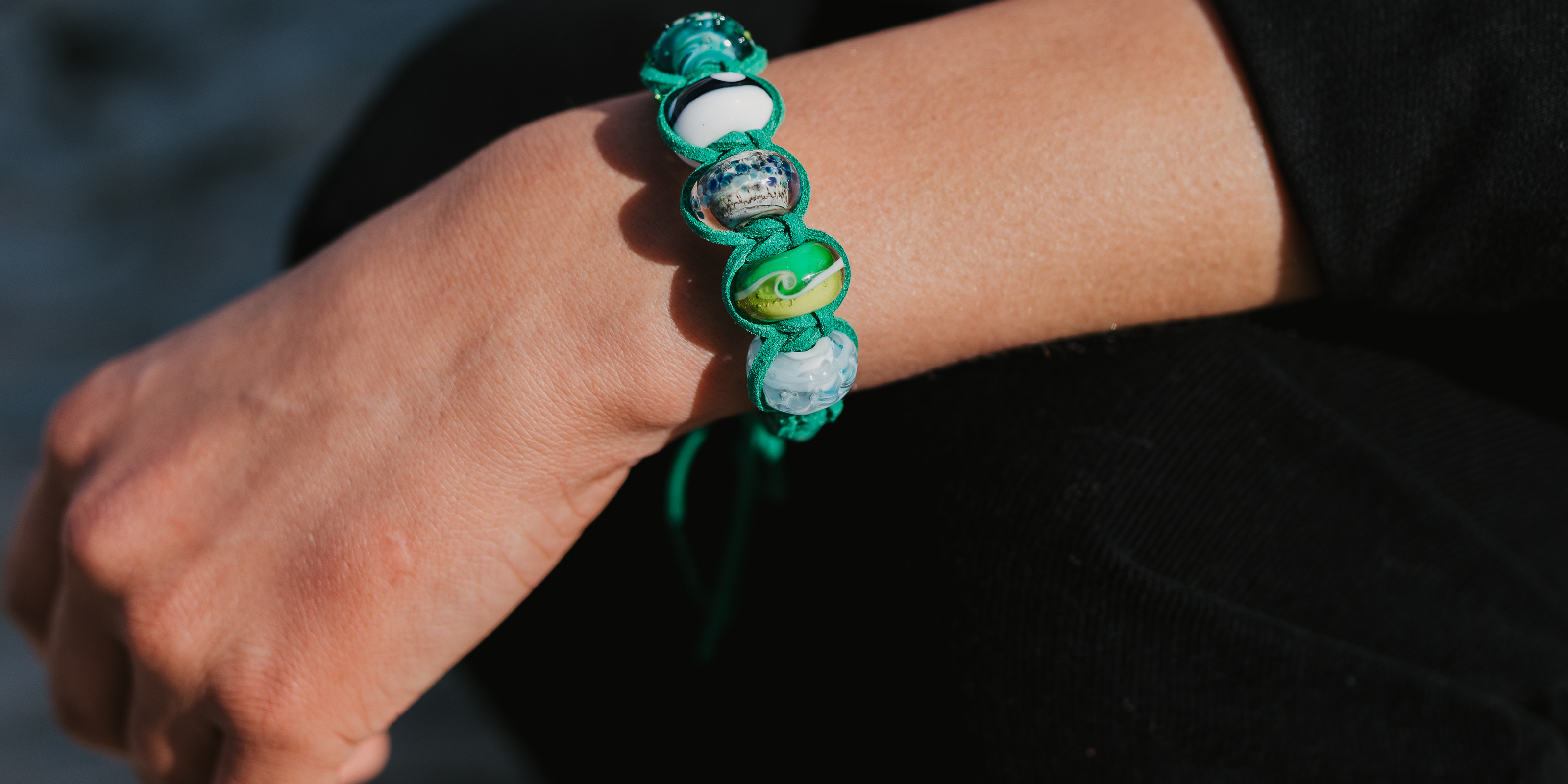 Person in black suit wearing a macramé green bracelet with glass beads.