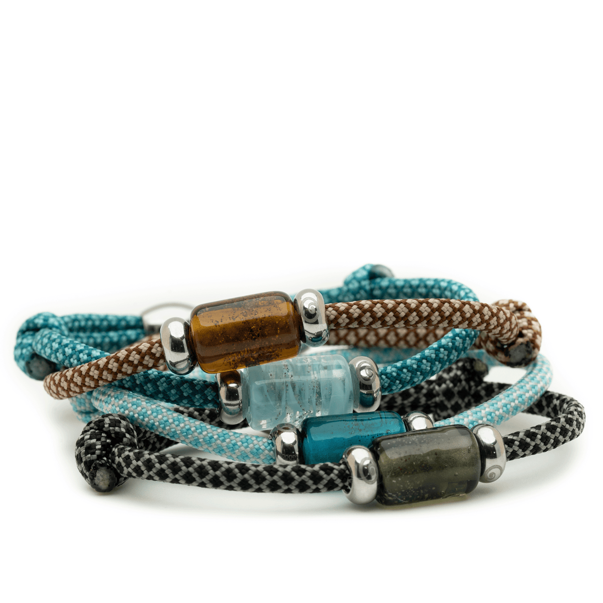 Four woven cord bracelets stacked together on a white background, featuring brown, teal, aqua, and black braided cords with metallic silver beads and cylindrical stone accents.