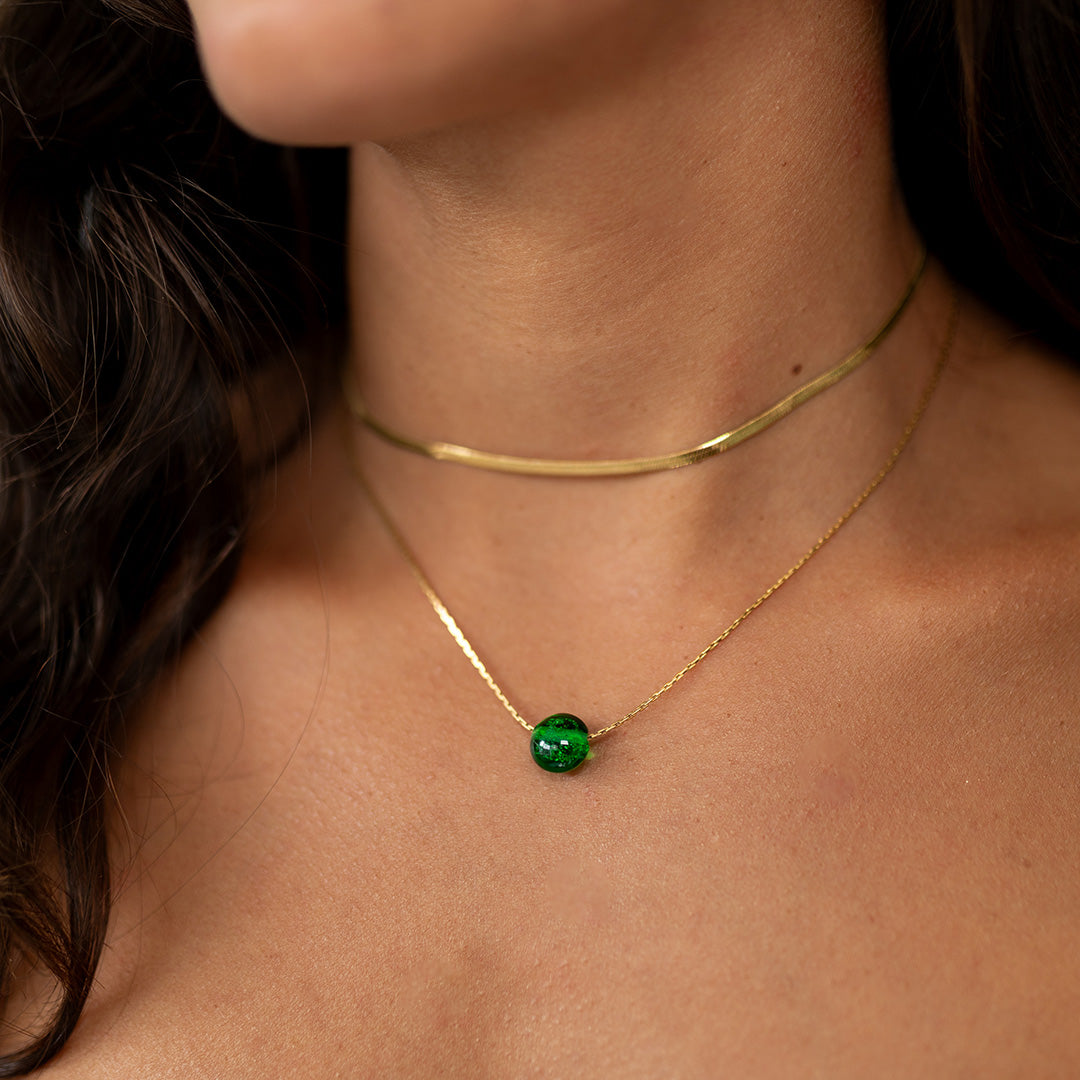 Emerald green sand pebble gold necklace worn by dark haired woman.