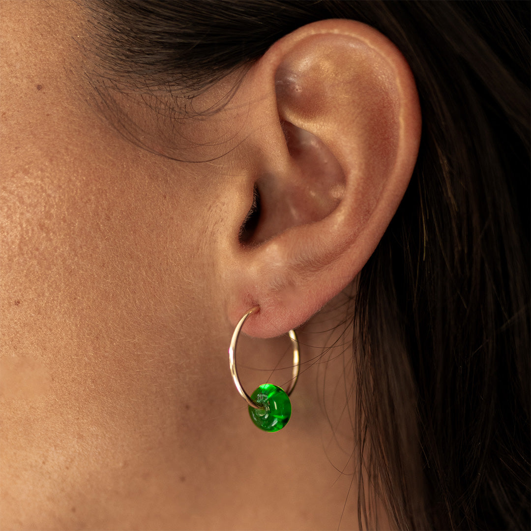 Woman wearing small gold hoop earring with green glass bead.