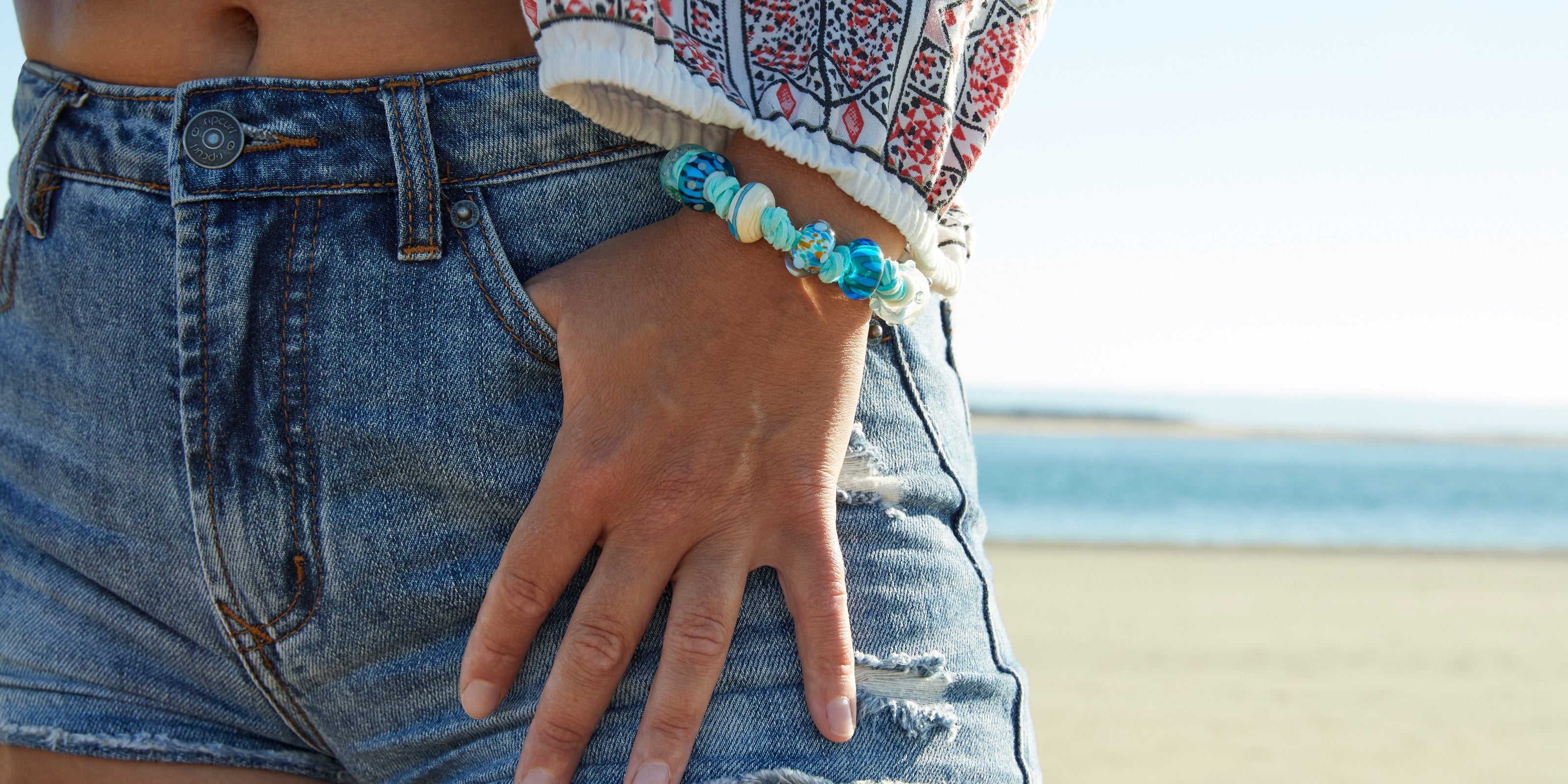 Mint colour vegan cord beaded bracelet worn by girl in denim shorts on Saunton Beach.