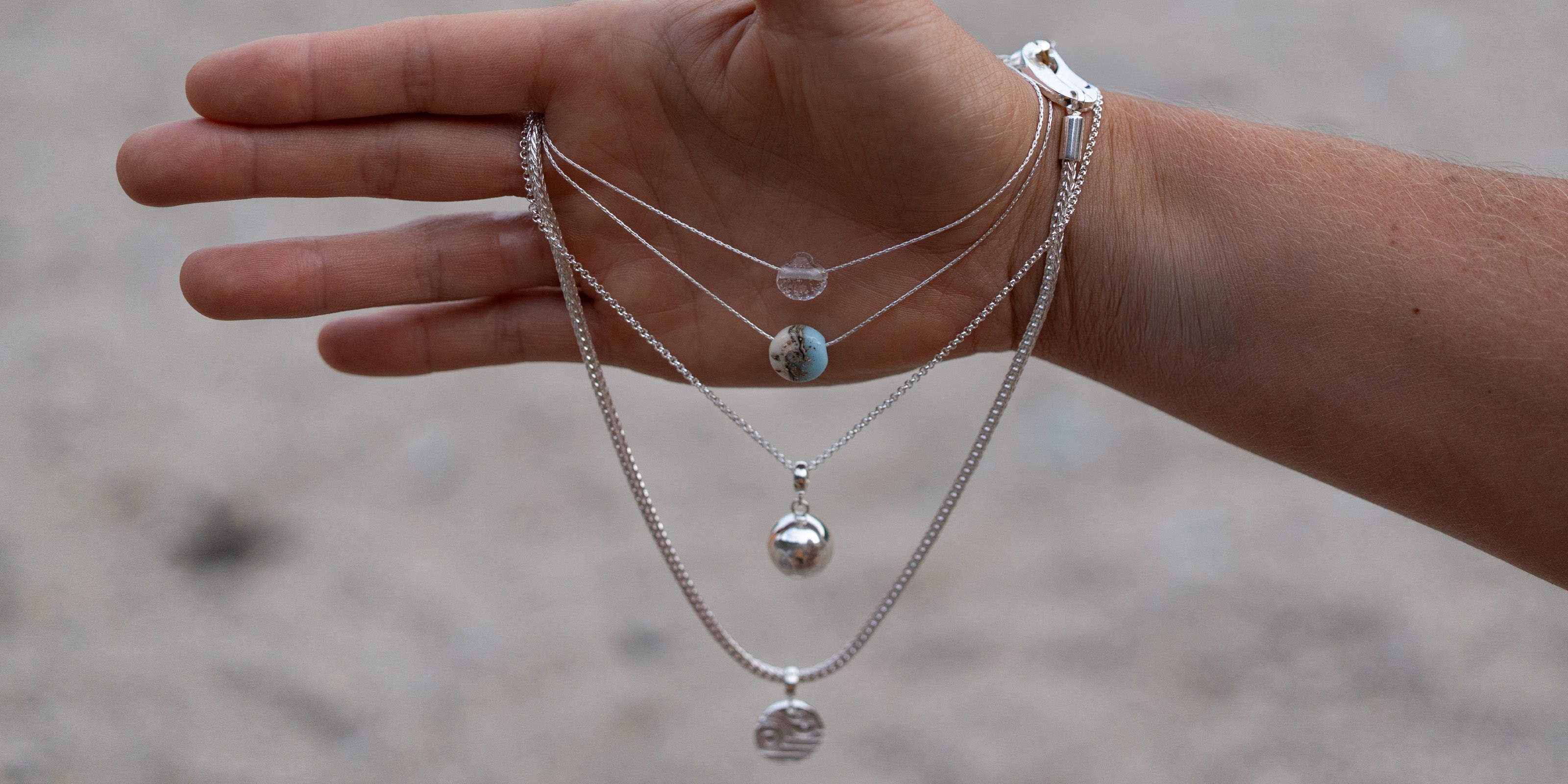 Hand wearing multiple silver necklaces with pendants against a blurred background