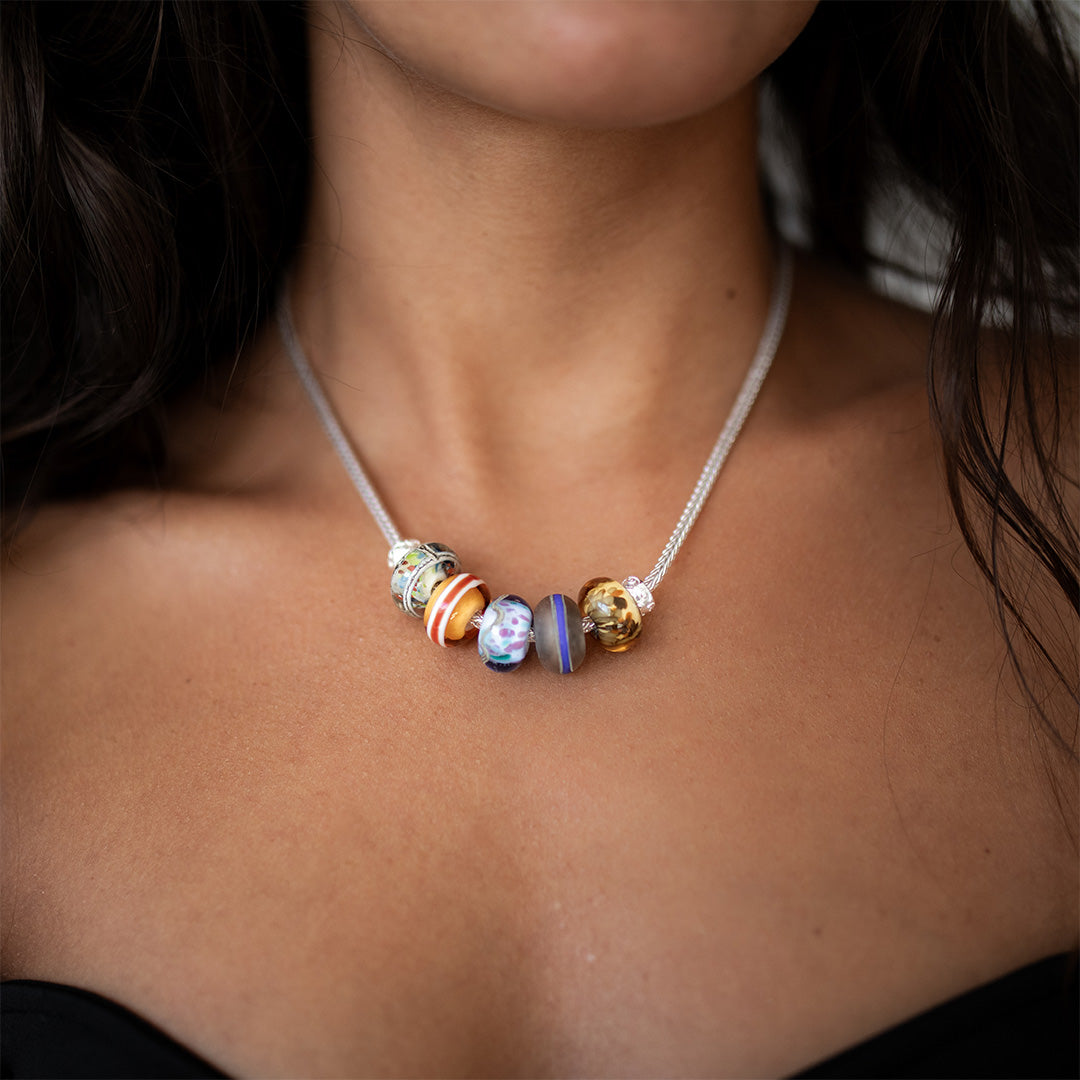 Dark haired woman wearing a chunky silver chain necklace with glass beads on it.