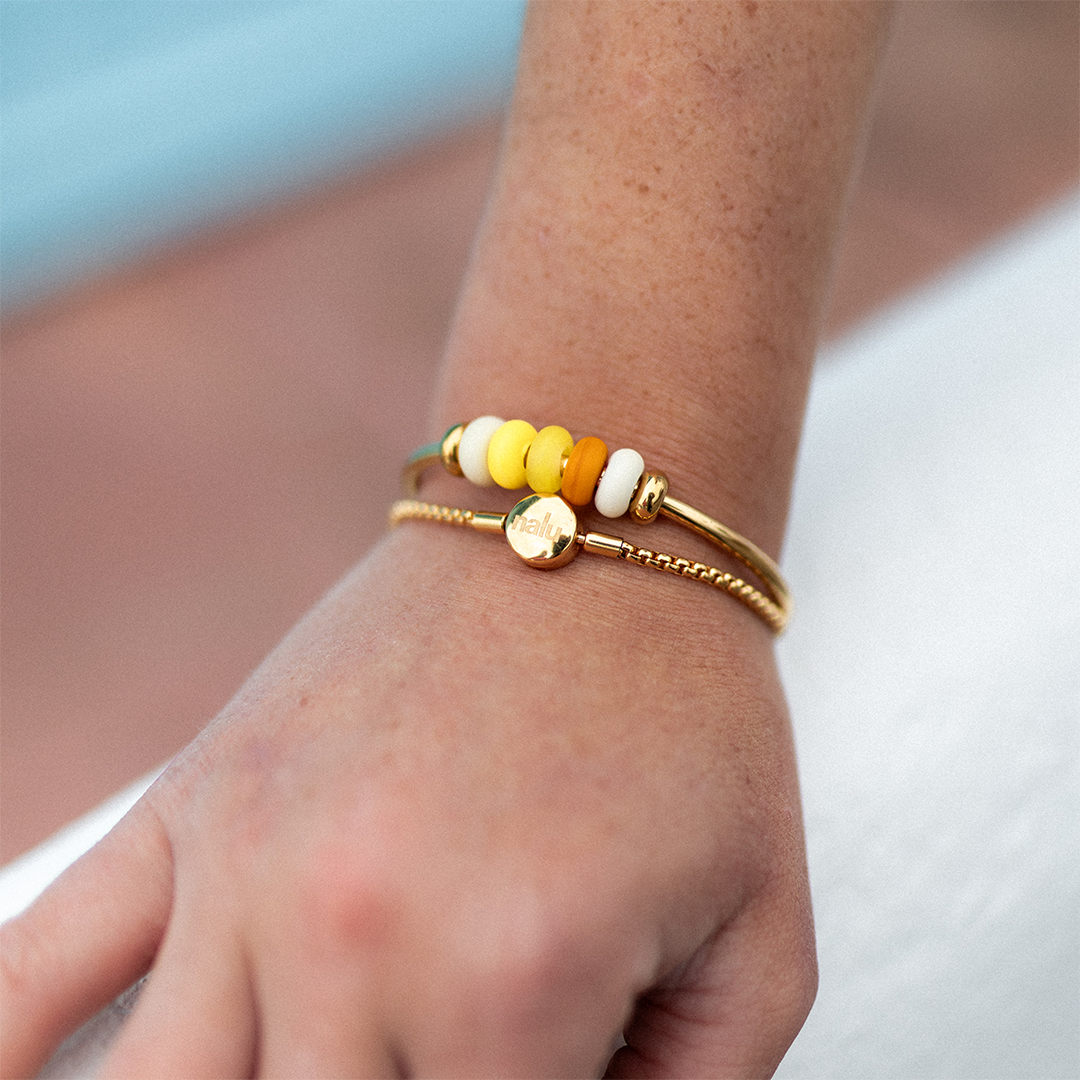 person wearing gold bangle with shades of yellow glass beads and old bracelet.