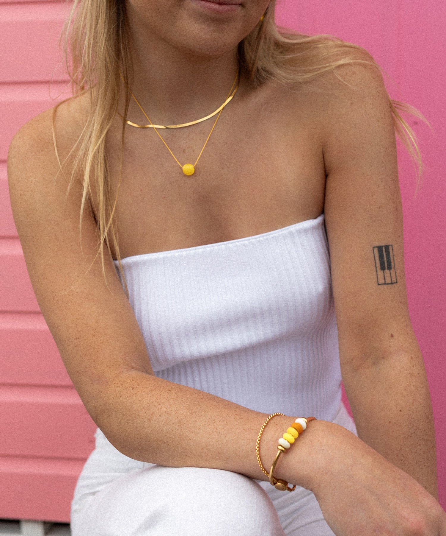 Woman wearing gold bracelets and necklace against pink beach house.