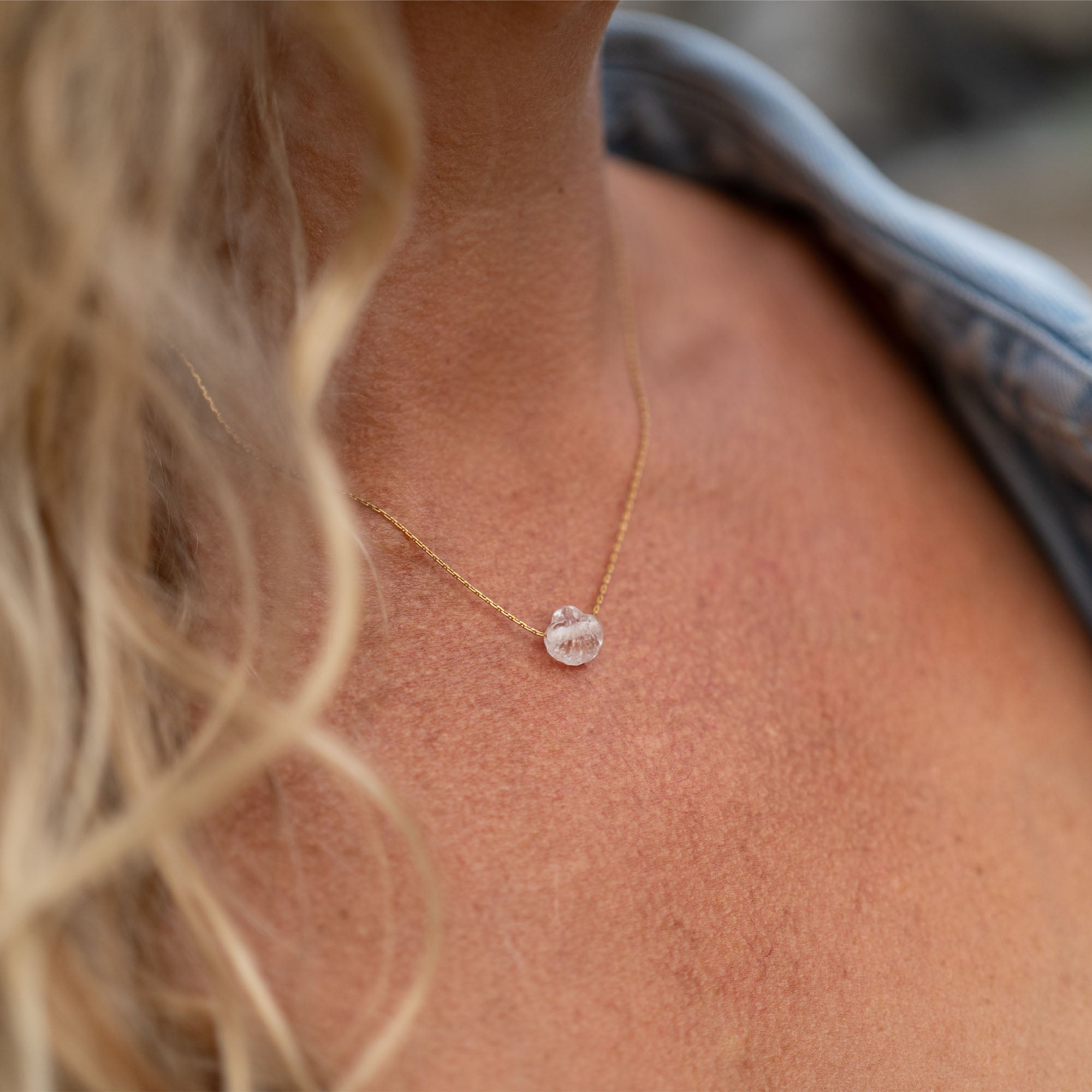 Necklace with a clear pendant worn by a person with blonde hair.