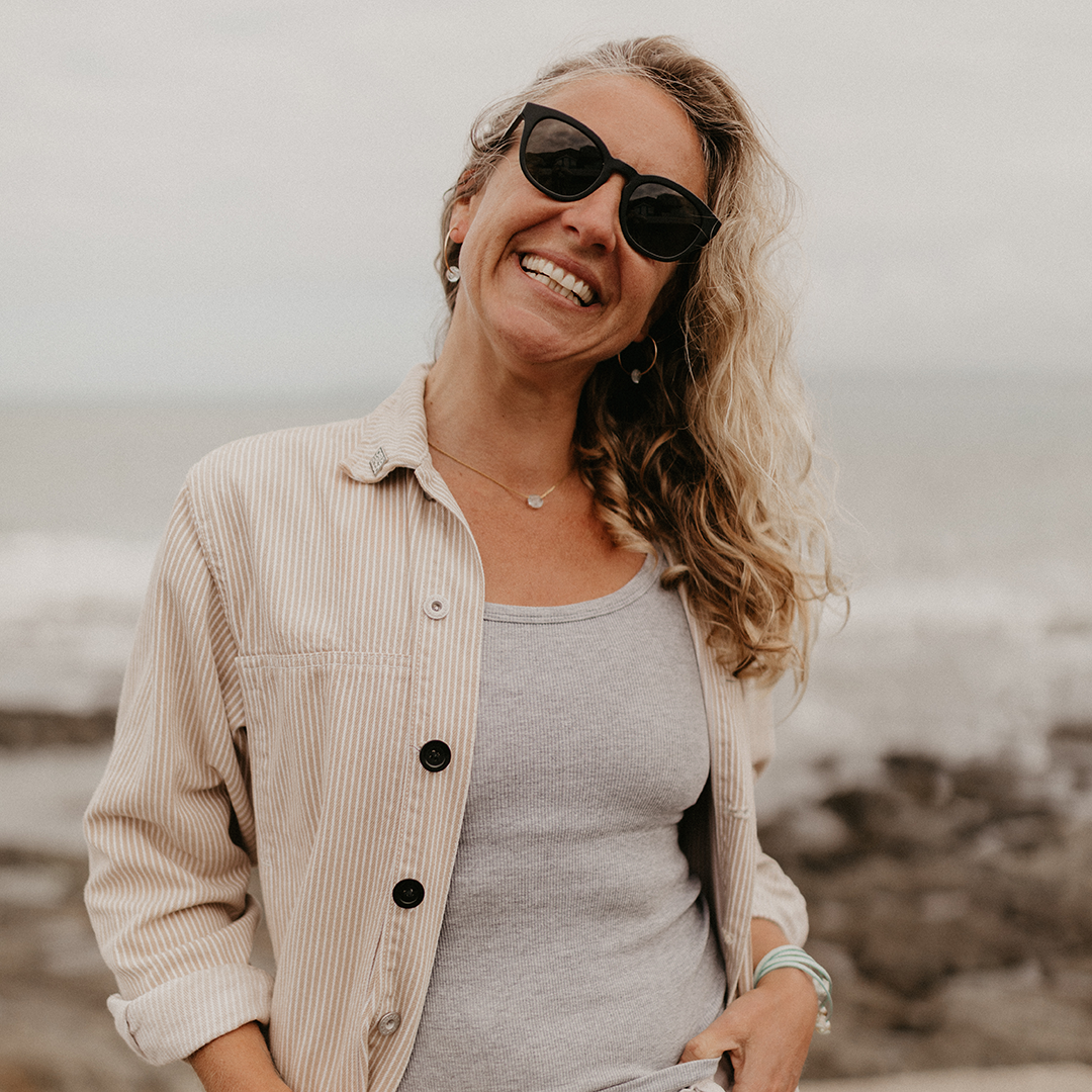 Woman at the beach in cream colour jacket wearing beach jewellery.