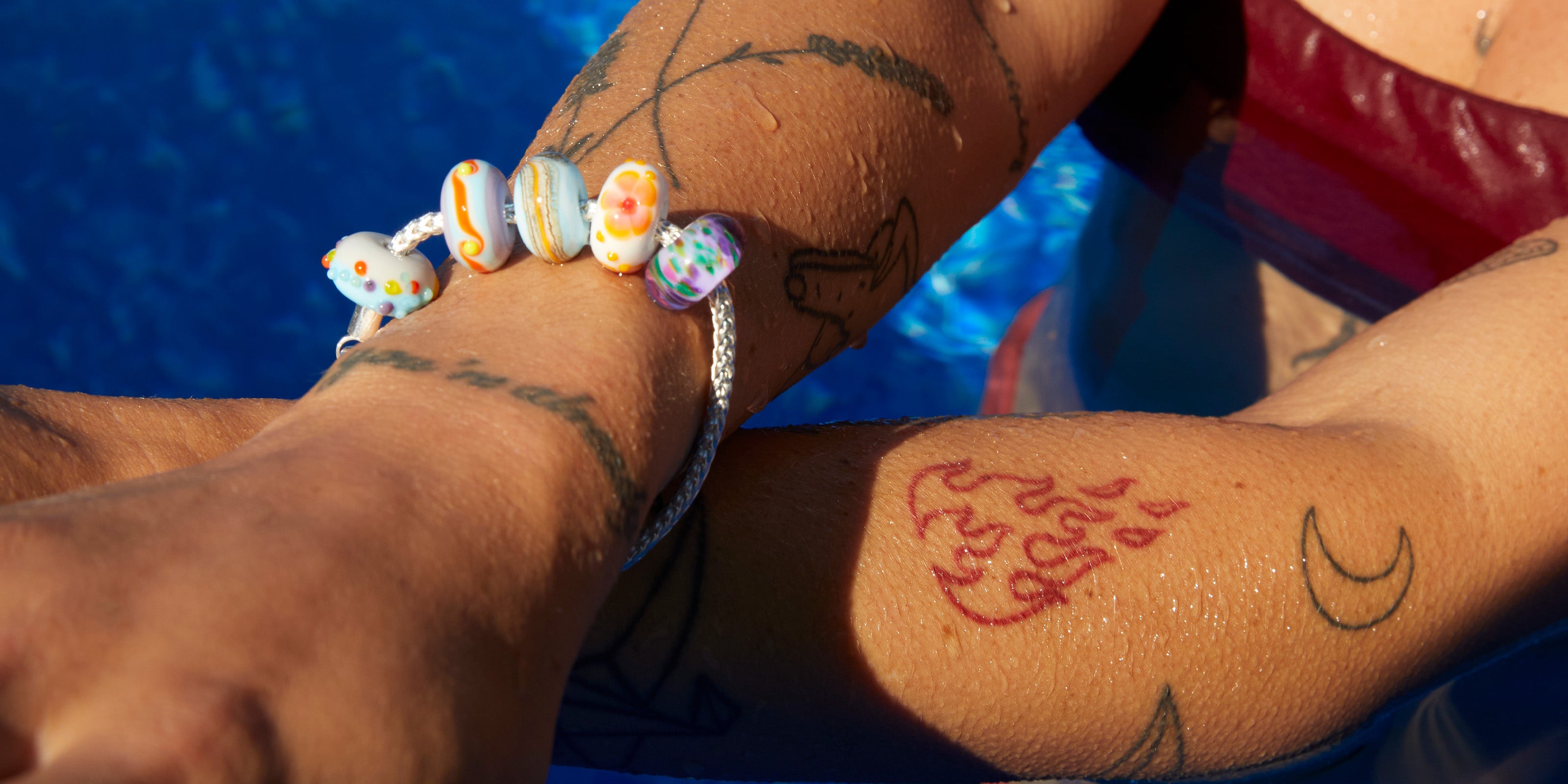 Colourful glass beads on silver tulang naga bracelet worn by woman in pool on holiday.