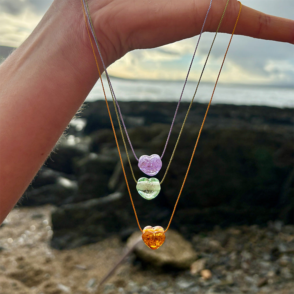 Colourful glass heart shaped pendant necklaces again a natural background.