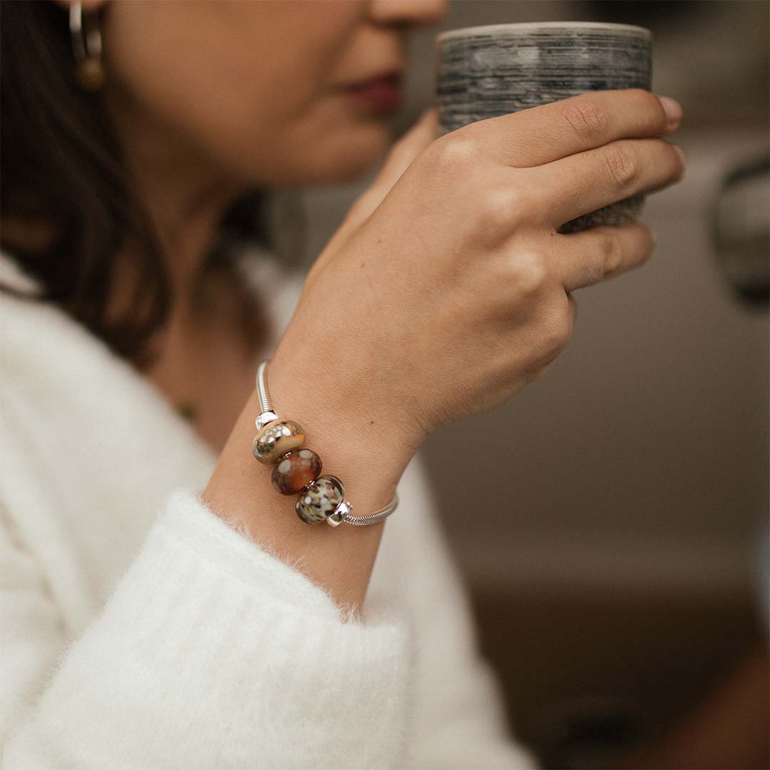 Woman drinking coffee wearing a silver bracelet with glass national park beads by Nalu.