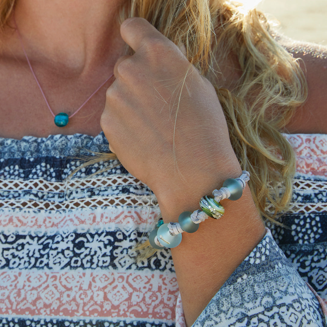 Girl wearing knotted bead cord bracelet with pink and blue top.