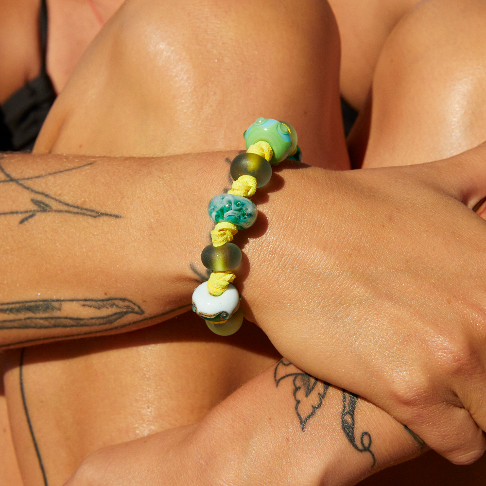 Person wearing yellow cord bracelet with patterned green and grey glass beads.