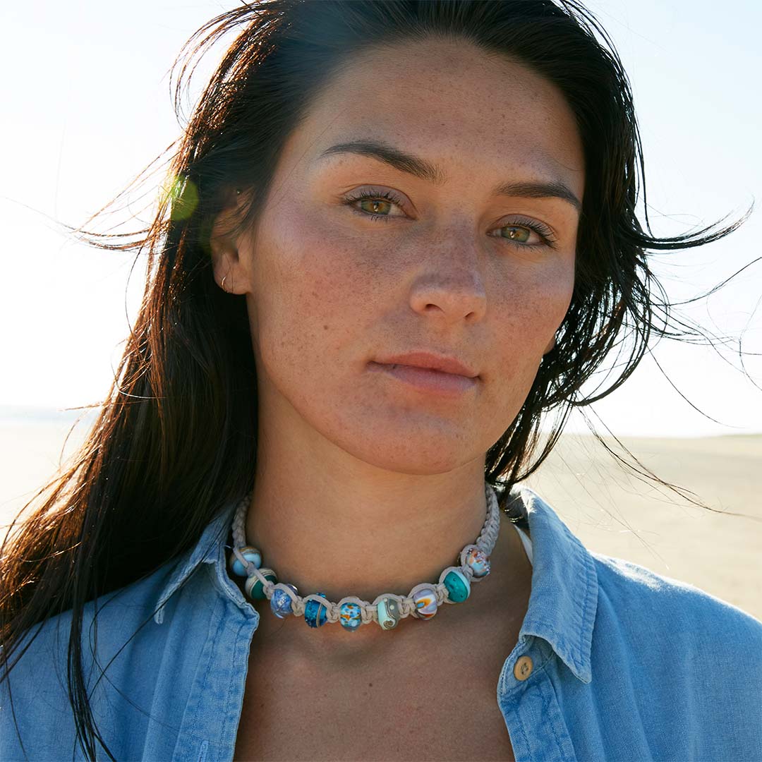 Dark haired woman in denim shirt wearing a grey cord choker necklace with various colour/patterned glass travel beads.