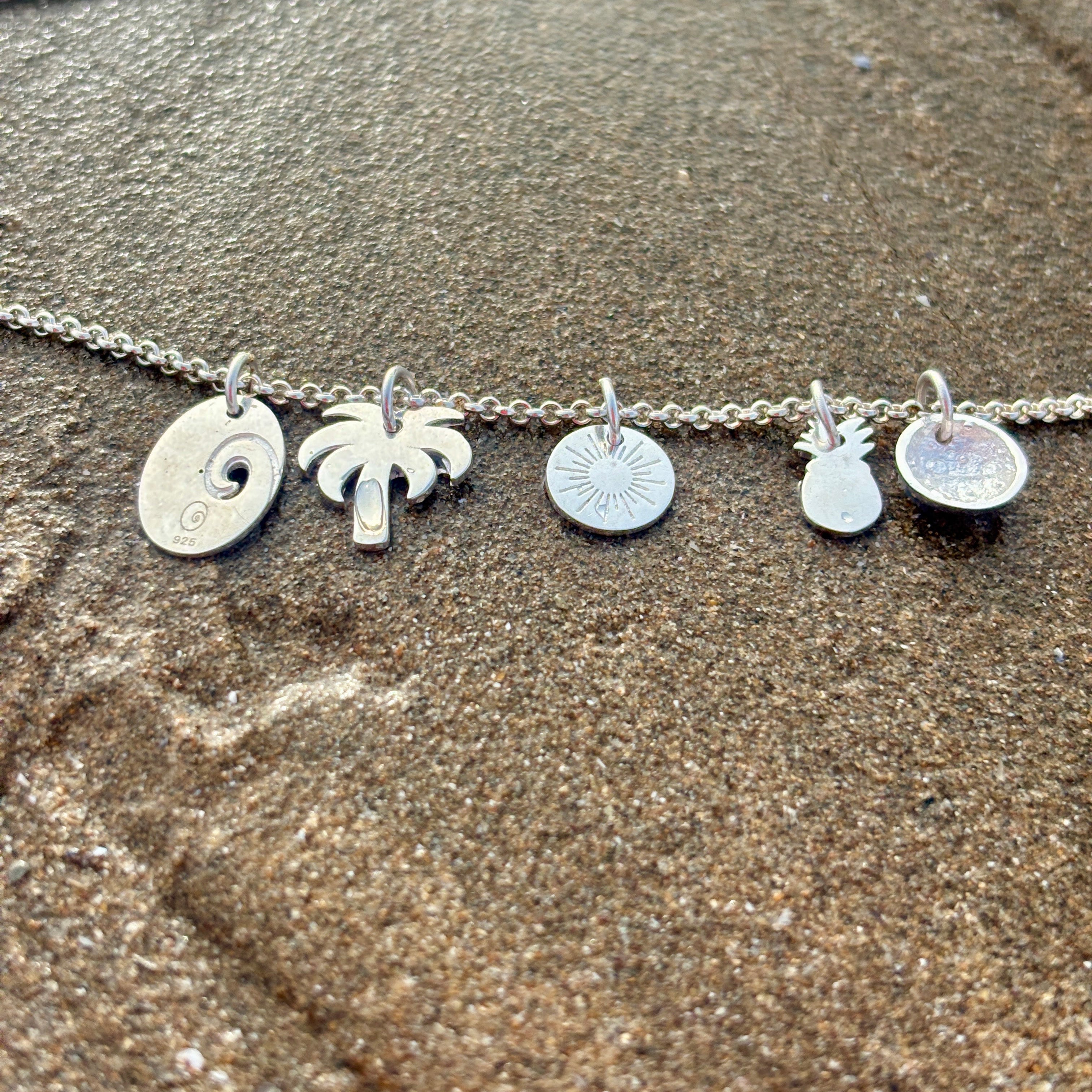 Silver necklace with beach-themed charms on a sandy surface
