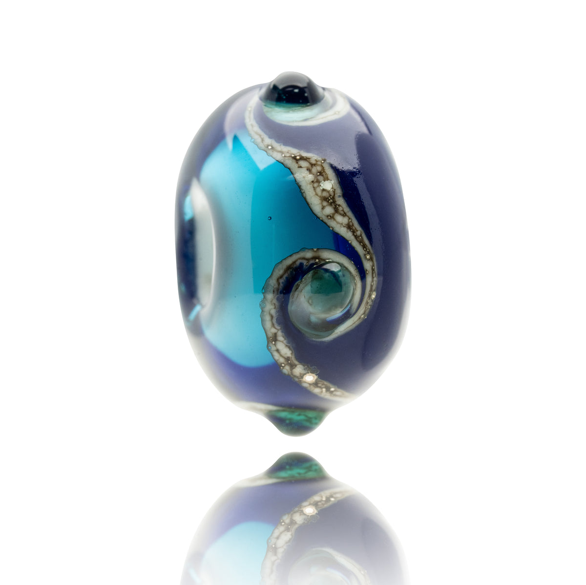 A single oval glass lampwork bead with a deep navy blue base, vibrant turquoise blue swirls, and metallic silver decorative patterns, shown on a reflective white surface.