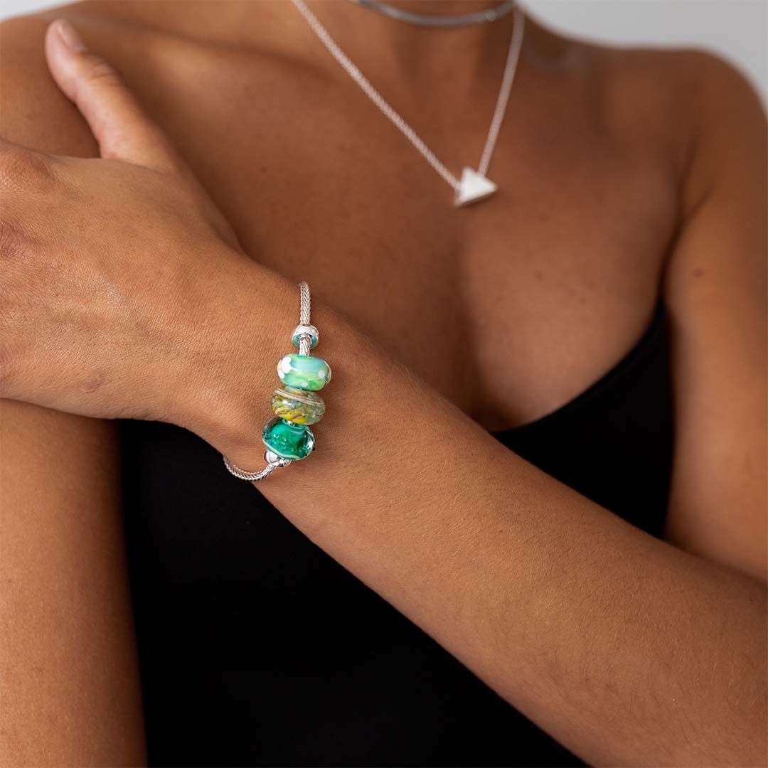 Woman wearing a black vest wearing a sterling silver bracelet with blue, green patterned glass beads.