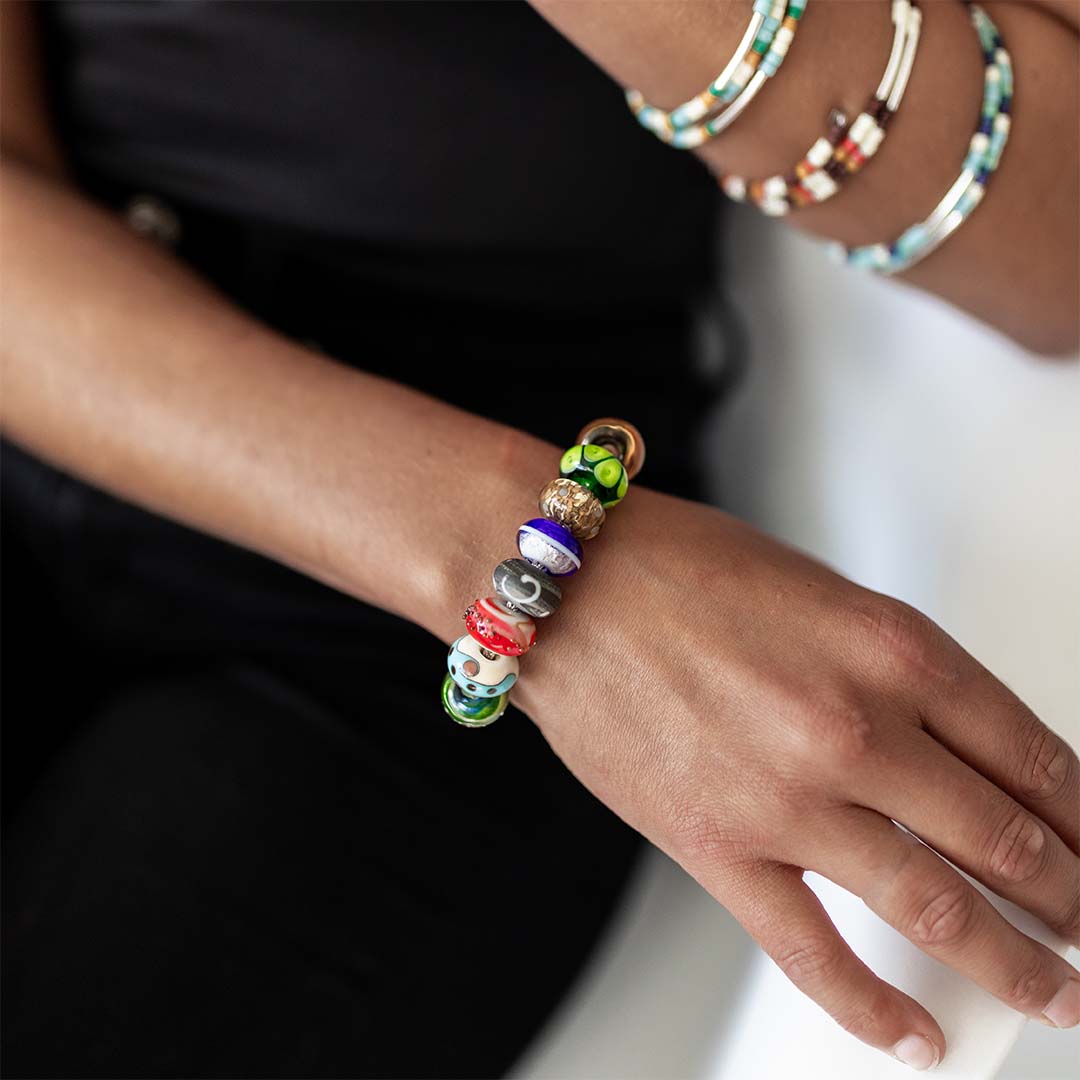 Person wearing a colourful beaded glass bead bracelet on a silver chain.