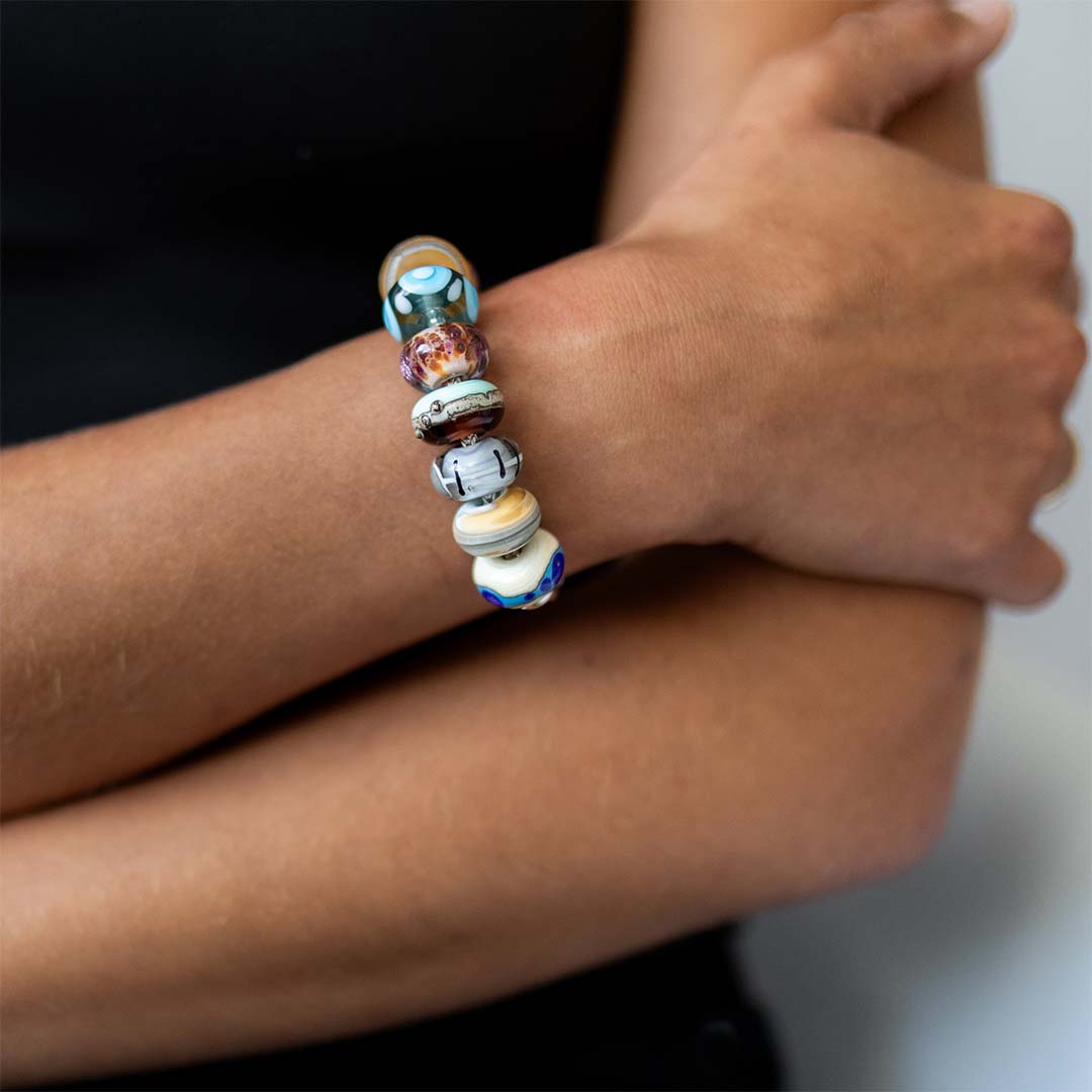 Coloured, pattered glass beads representing UK holiday destinations on silver bracelet worn by woman.