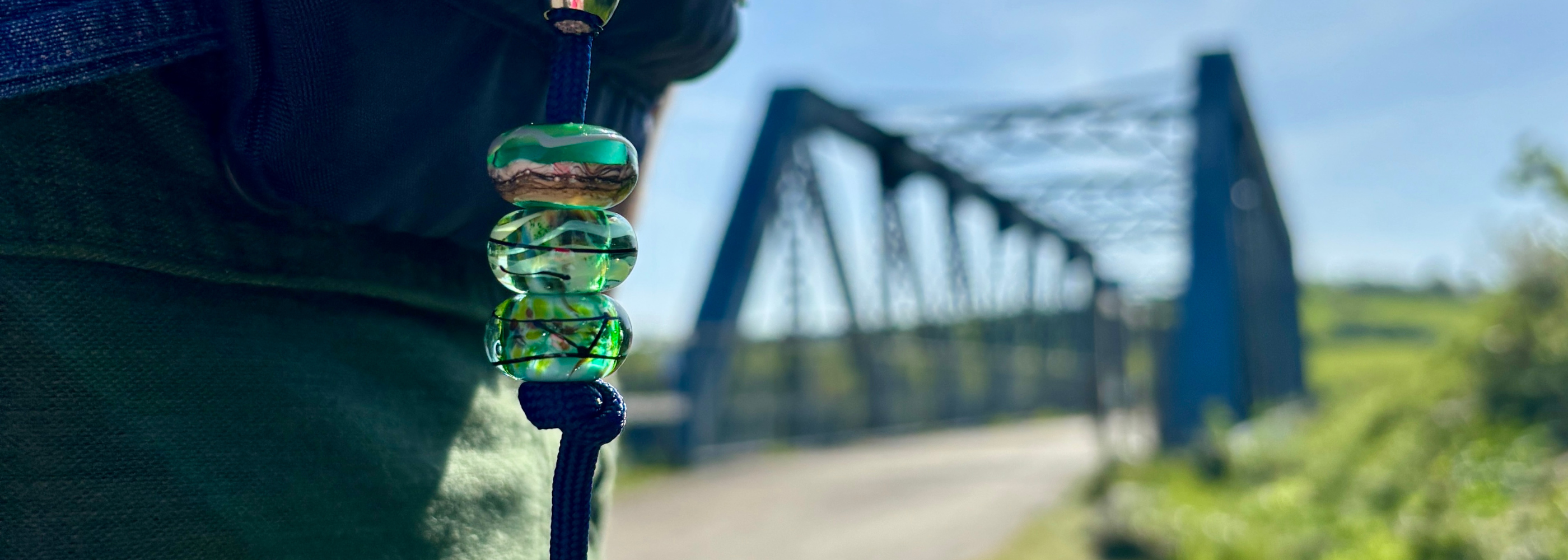 Green glass bead on a cord with a blurred bridge and blue sky in the background