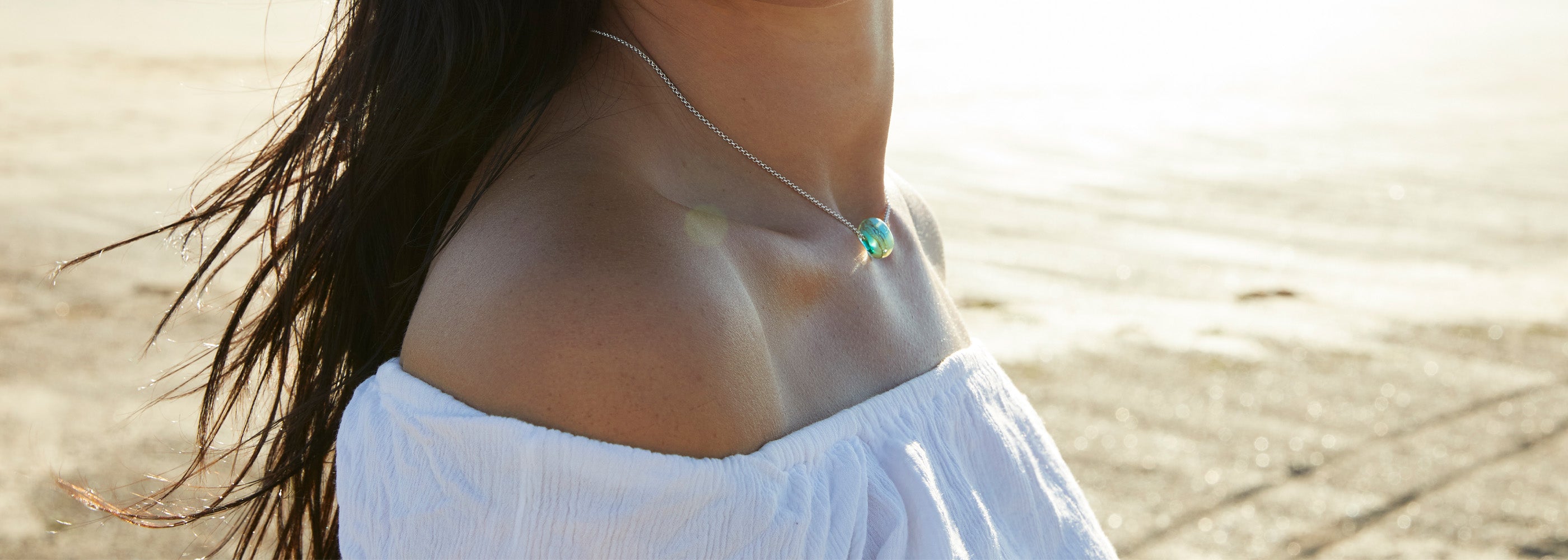Woman on beach wearing a glass Pedn Vounder bead on silver chain necklace.