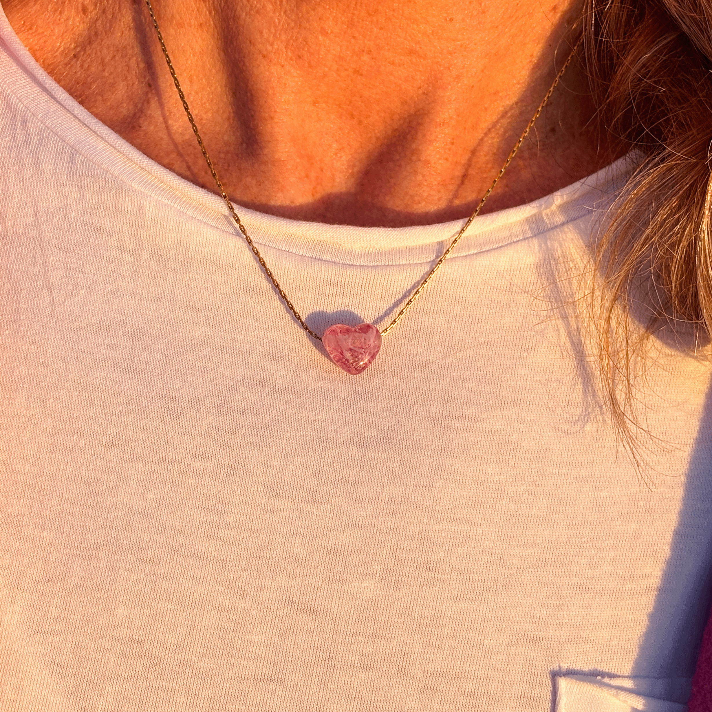 Pink sand heart necklace on gold chain worn by person.