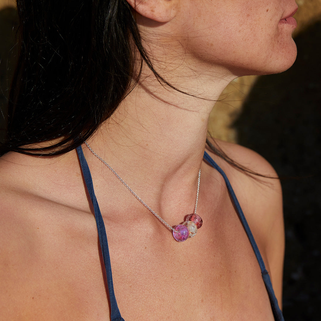 Pink beach sand trio necklace worn by dark haired woman.