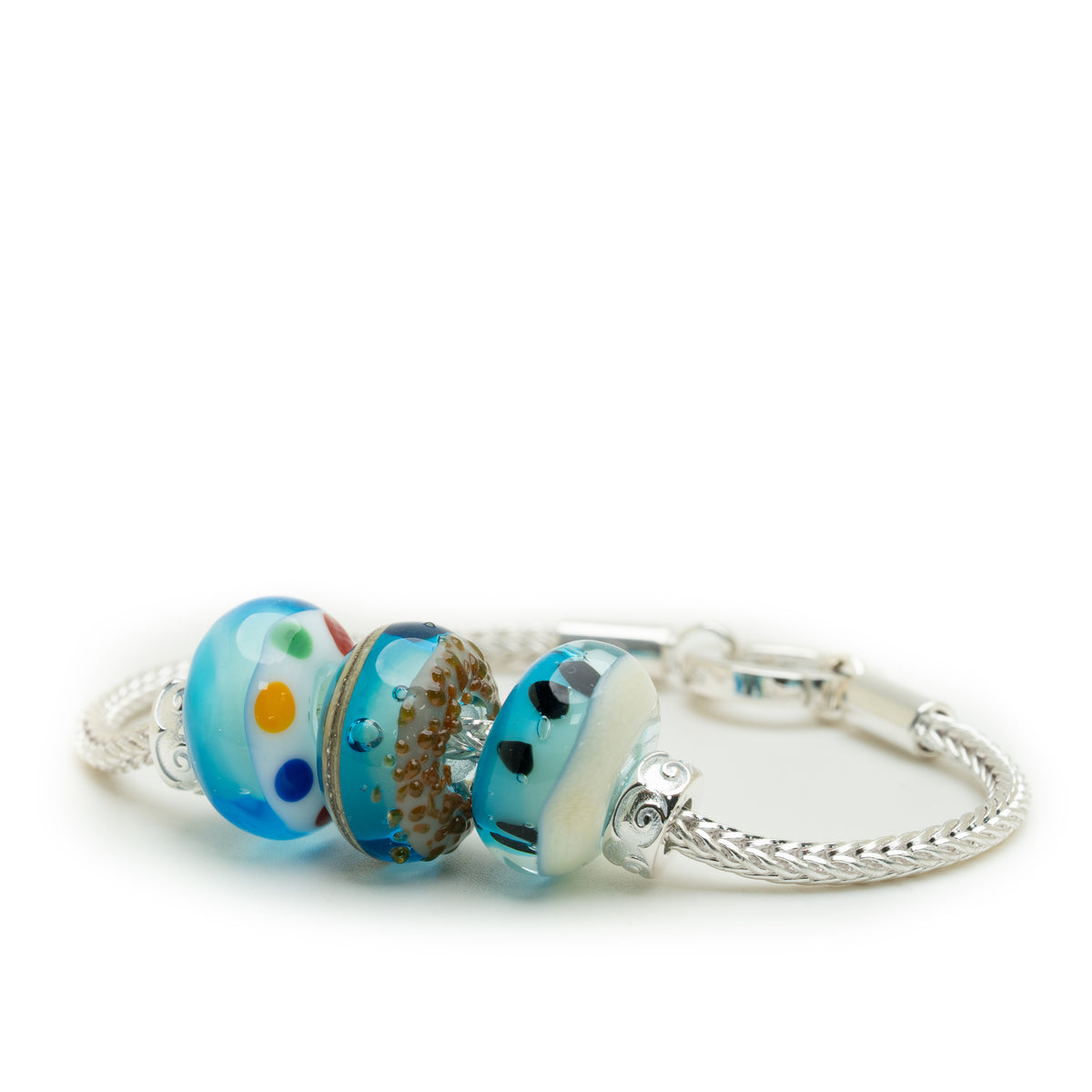 A silver-toned bangle bracelet featuring three decorative glass lampwork beads in shades of blue, white, brown, and small colorful accents, displayed on a clean white background.