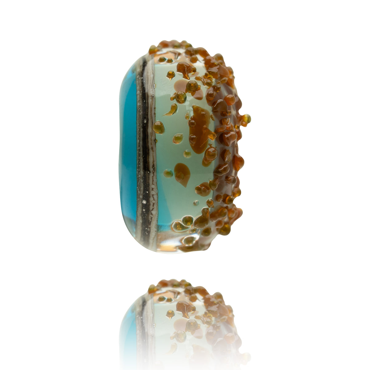 A handmade glass lampwork bead with a vibrant turquoise blue section, a pale mint green section, and a textured border of amber-brown bubble details, shown on a white background with a soft reflection below.